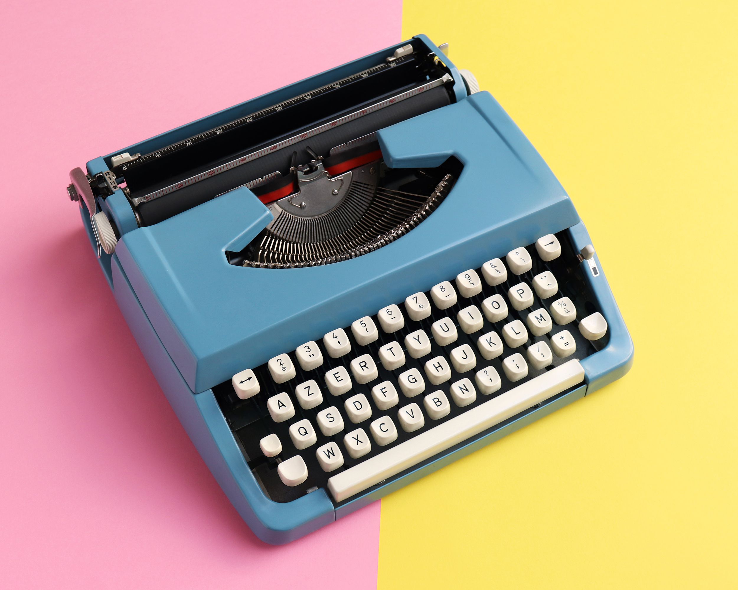 Vintage blue typewriter on a two-toned pastel background of pink and light yellow