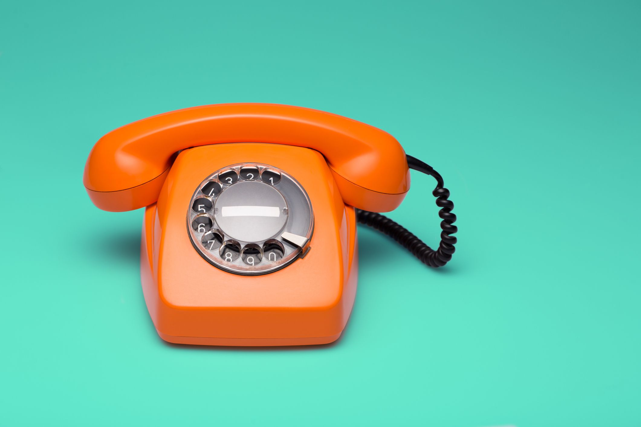 Vintage orange rotary phone with black cord on a blue-green background