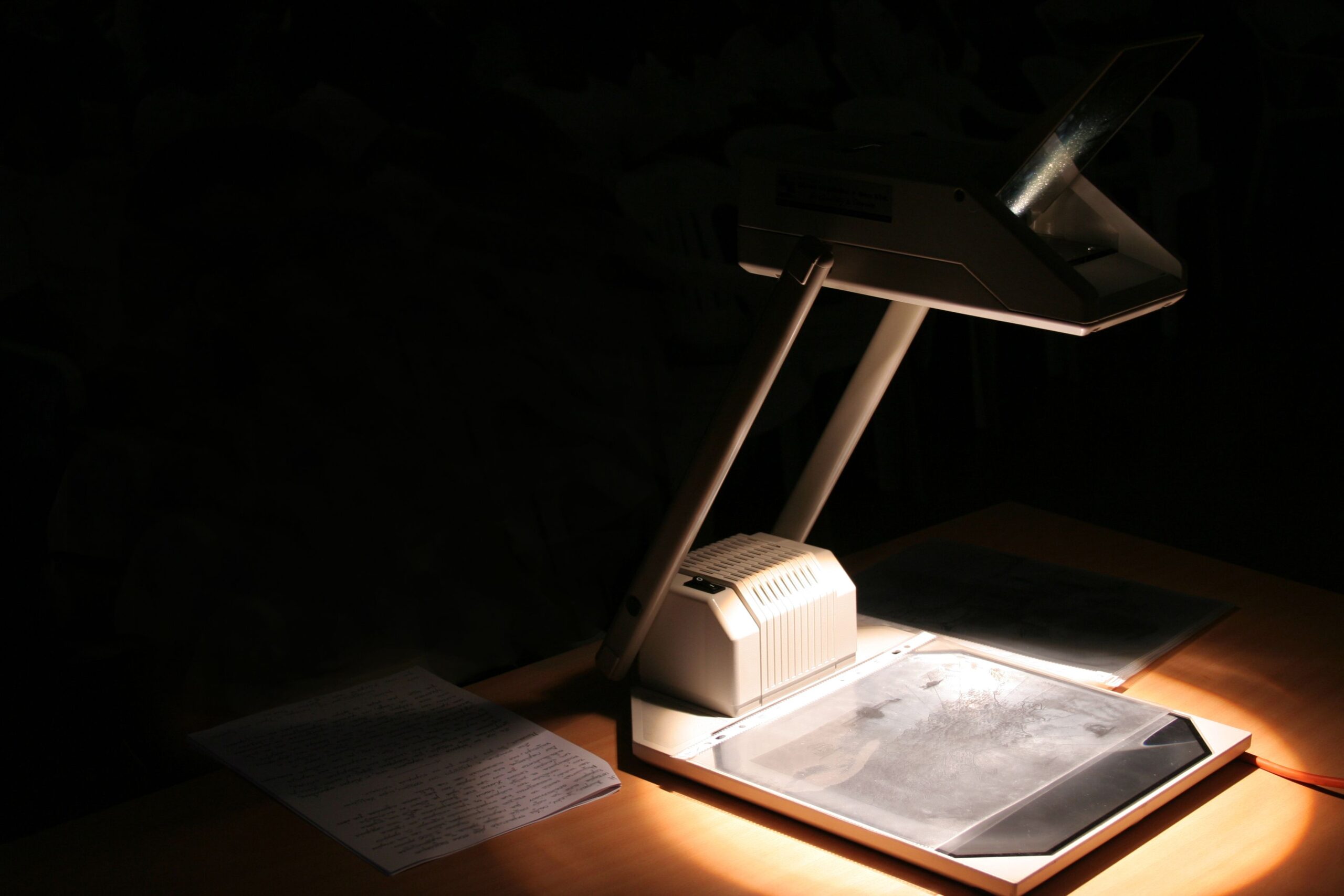 Vintage overhead projector with light shining, on a desk with papers close with a dark background
