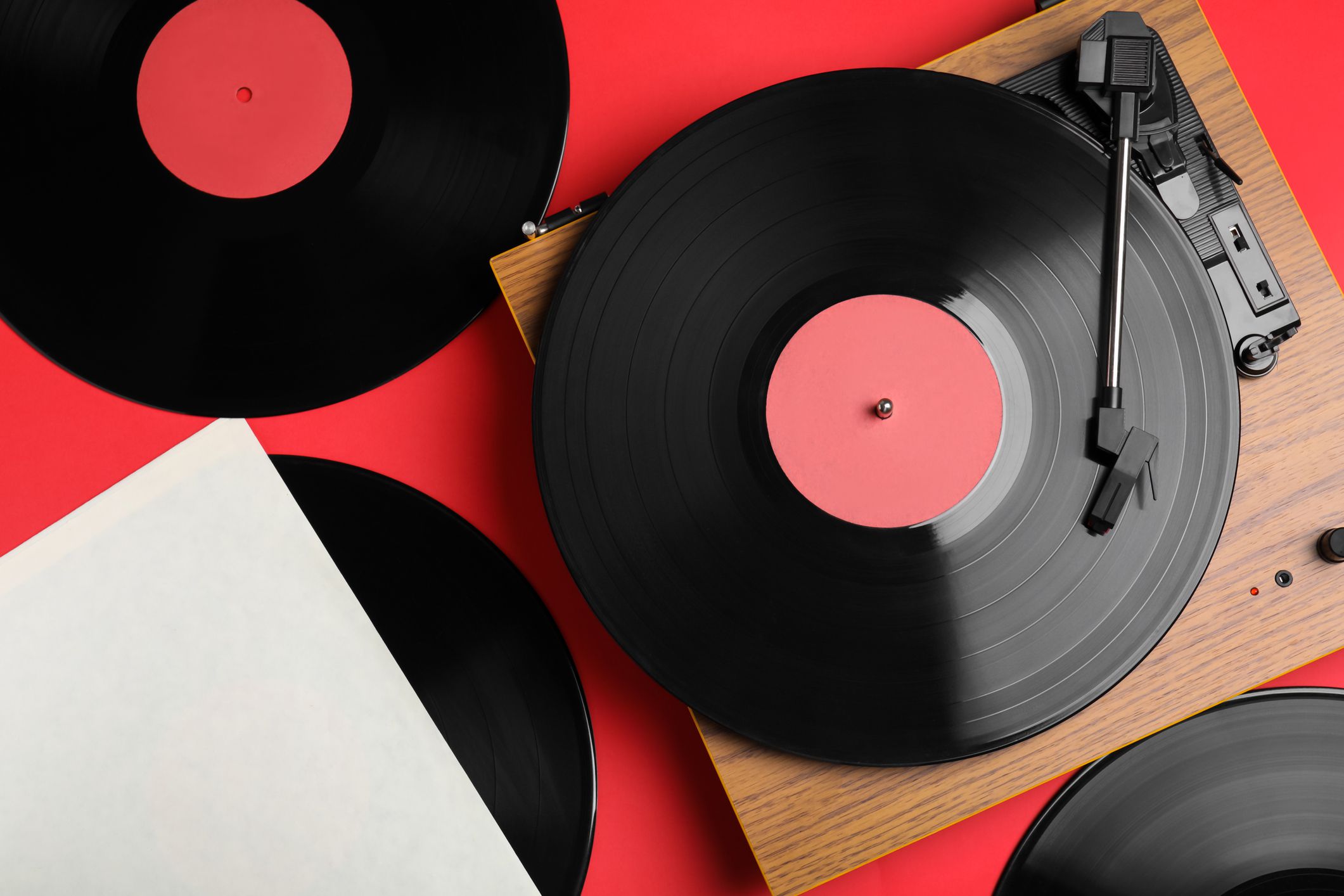 Vinyl record being played on a player with three records on a red background