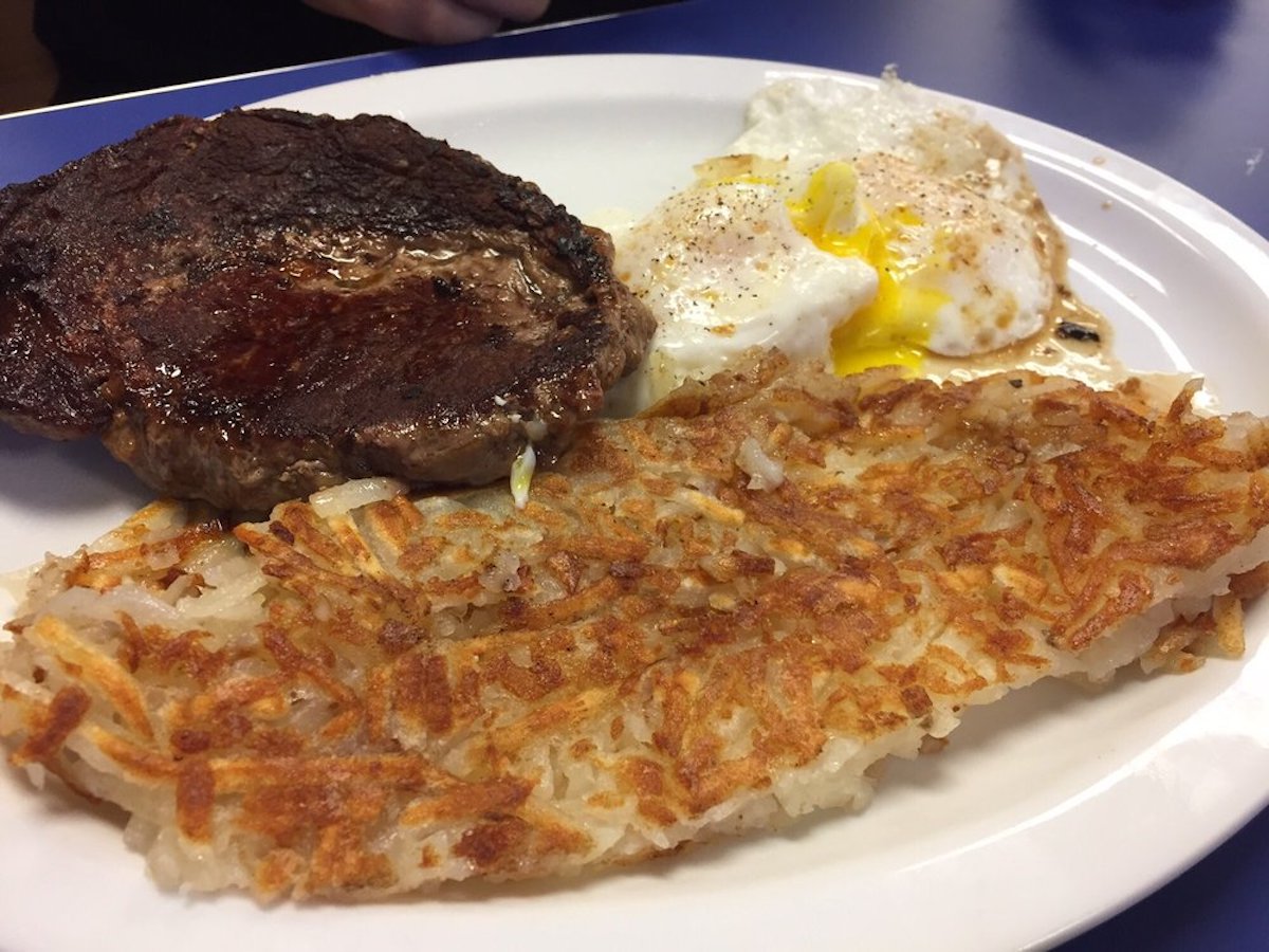 A plate with a cooked steak, two sunny-side-up eggs with runny yolks, and a serving of golden-brown hash browns.