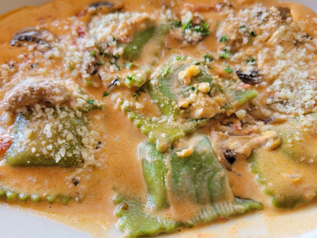Spinach ravioli covered in a creamy tomato sauce, topped with grated parmesan cheese and garnished with chopped herbs. Some mushroom slices are also visible in the sauce.
