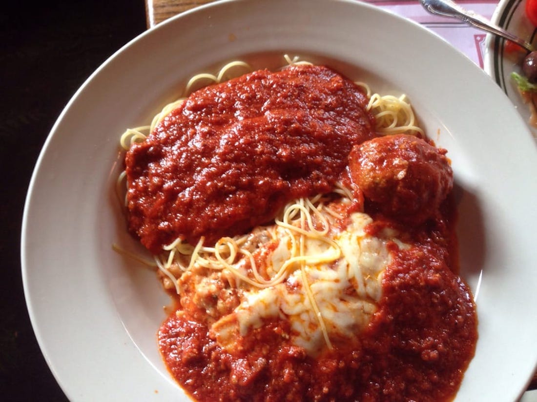 A plate of spaghetti topped with marinara sauce, melted cheese, and a meatball, served on a white dish.