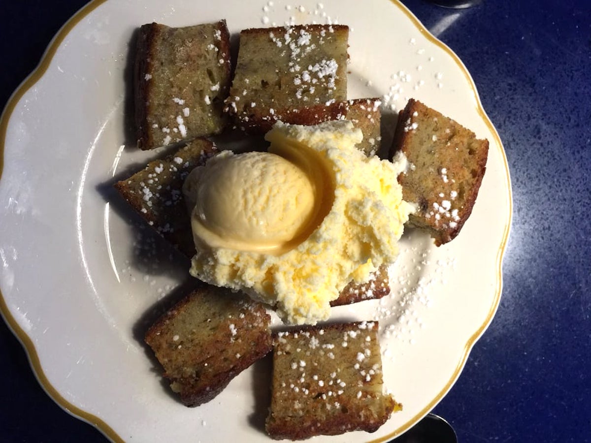 A plate with several square pieces of banana bread, topped with a scoop of vanilla ice cream and sprinkled with powdered sugar.