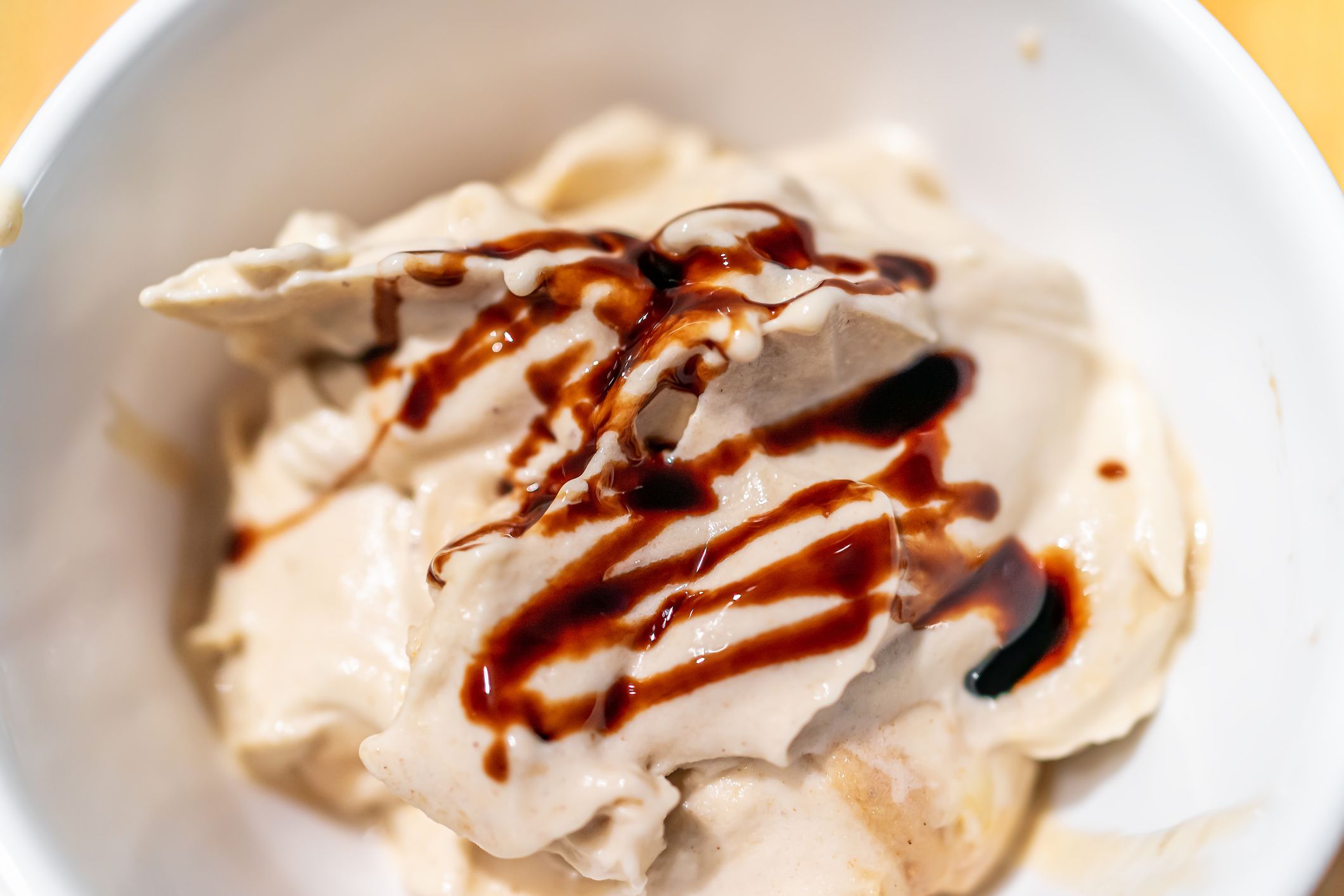 Soft serve vanilla ice cream macro closeup in bowl made from banana nice cream vegan dessert and drizzled balsamic vinegar syrup or chocolate sauce