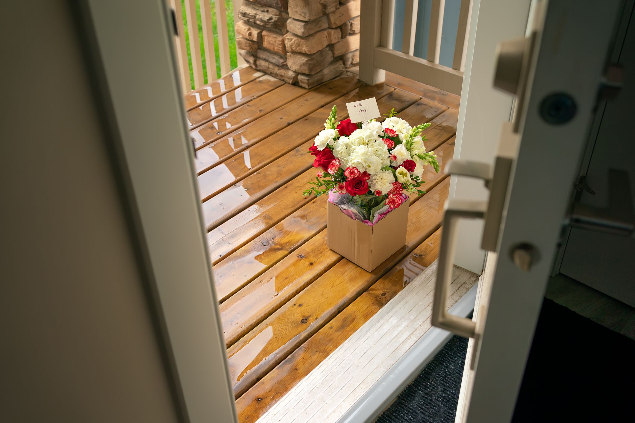 A bouquet of flowers in a carton box on a porch of a house through open door. Surprise contactless delivery of flowers for woman. Delivery of goods home during quarantine. A pleasant unexpected gift.