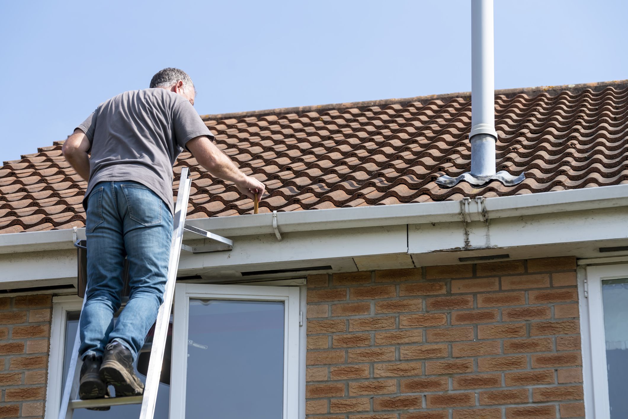 Senior man cleaning gutters on a suburban English house.