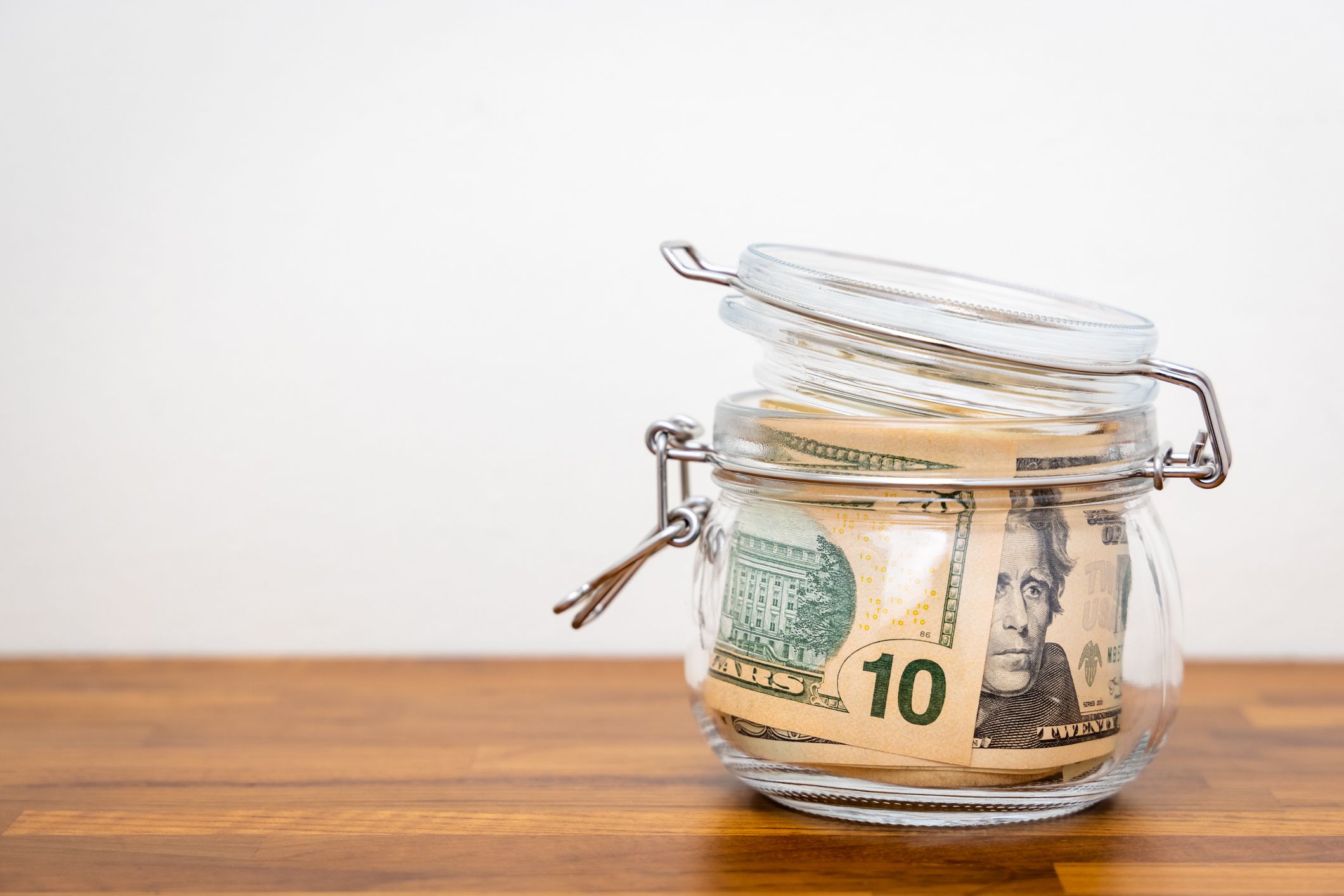 US Dollar cash banknote in a closed glass jar put on wooden table with white background. Money saving concept.