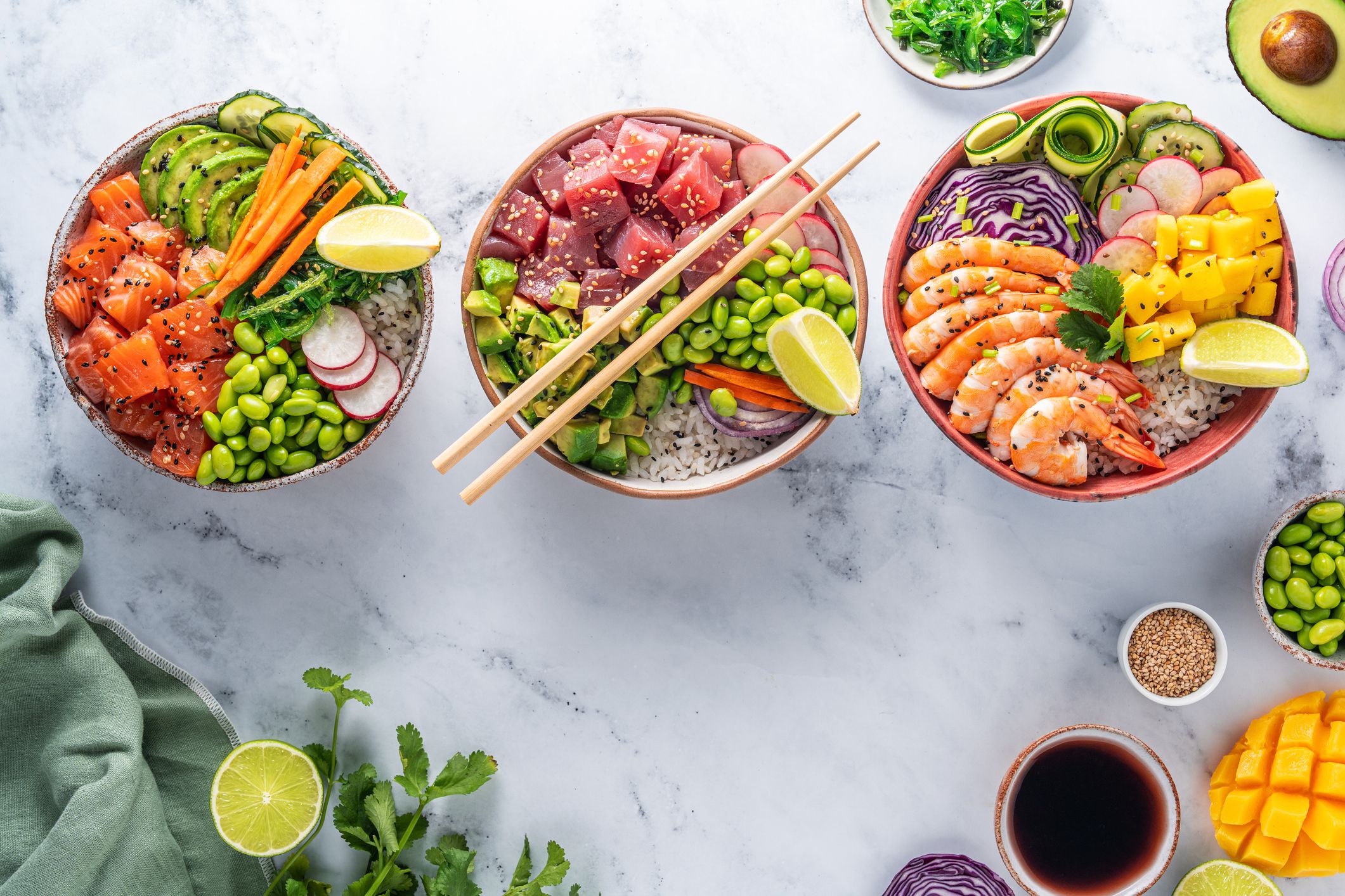 Poke bowls varied, salmon Poke, Tuna Poke and Shrimp Poke assorted on white marble background with ingredients and sauce