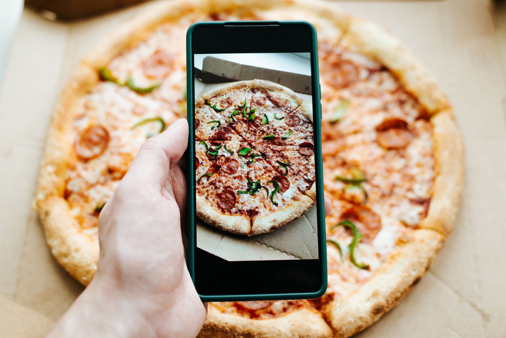 Person photographing pizza on mobile phone camera, close-up. Food photo.