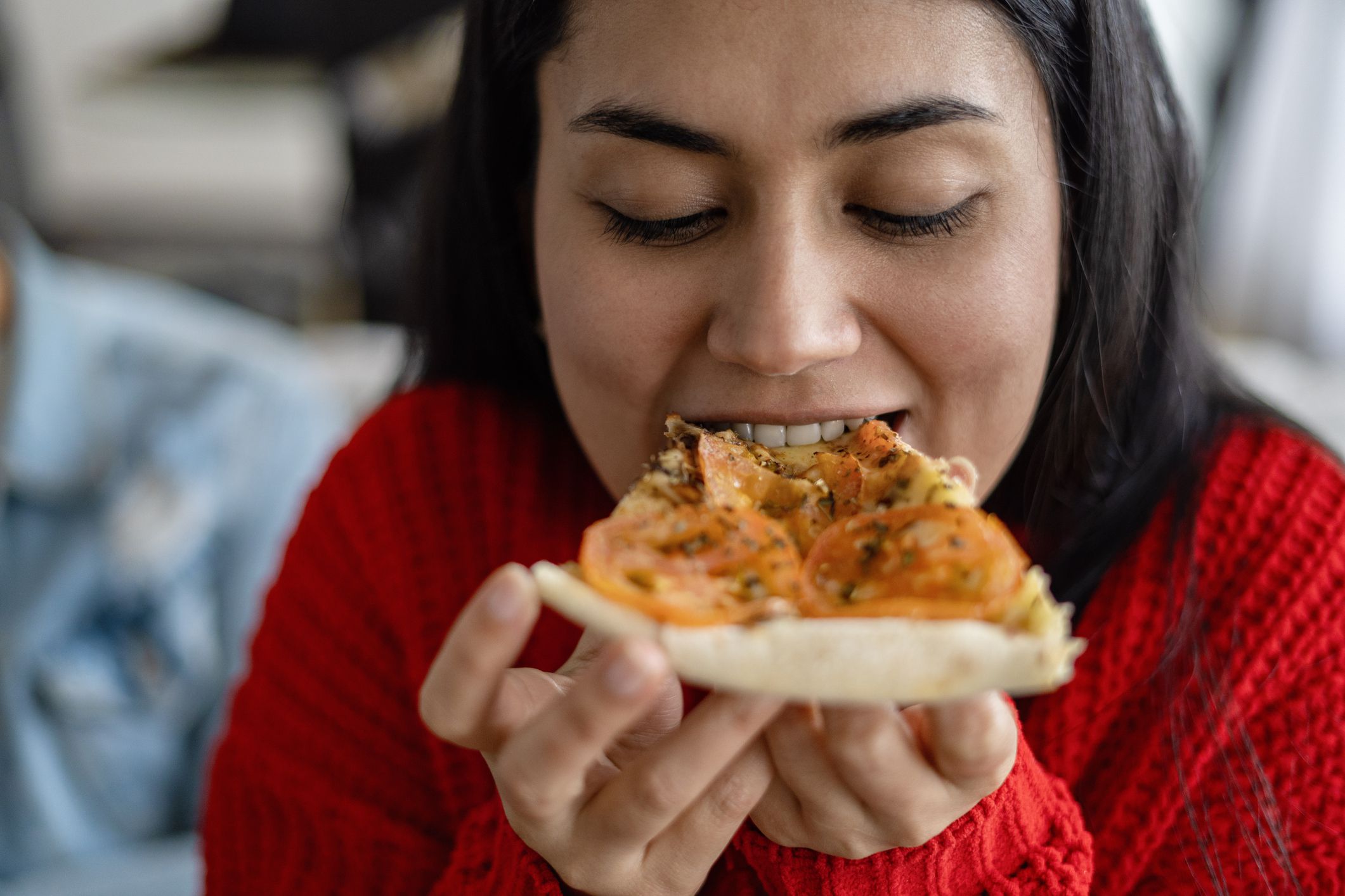 Portrait of a Latina woman eating pizza in her living room.