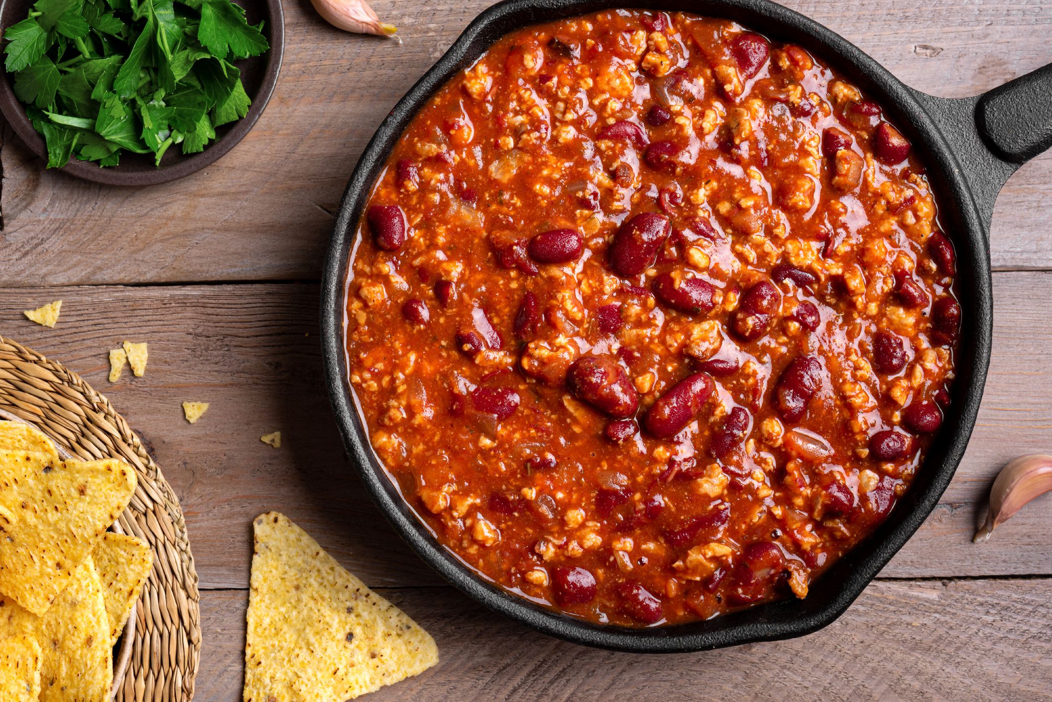 Chili con carne in pan on wooden background, top view. Homemade mexican food concept, chili with red beans and ground beef, protein fiber meal.