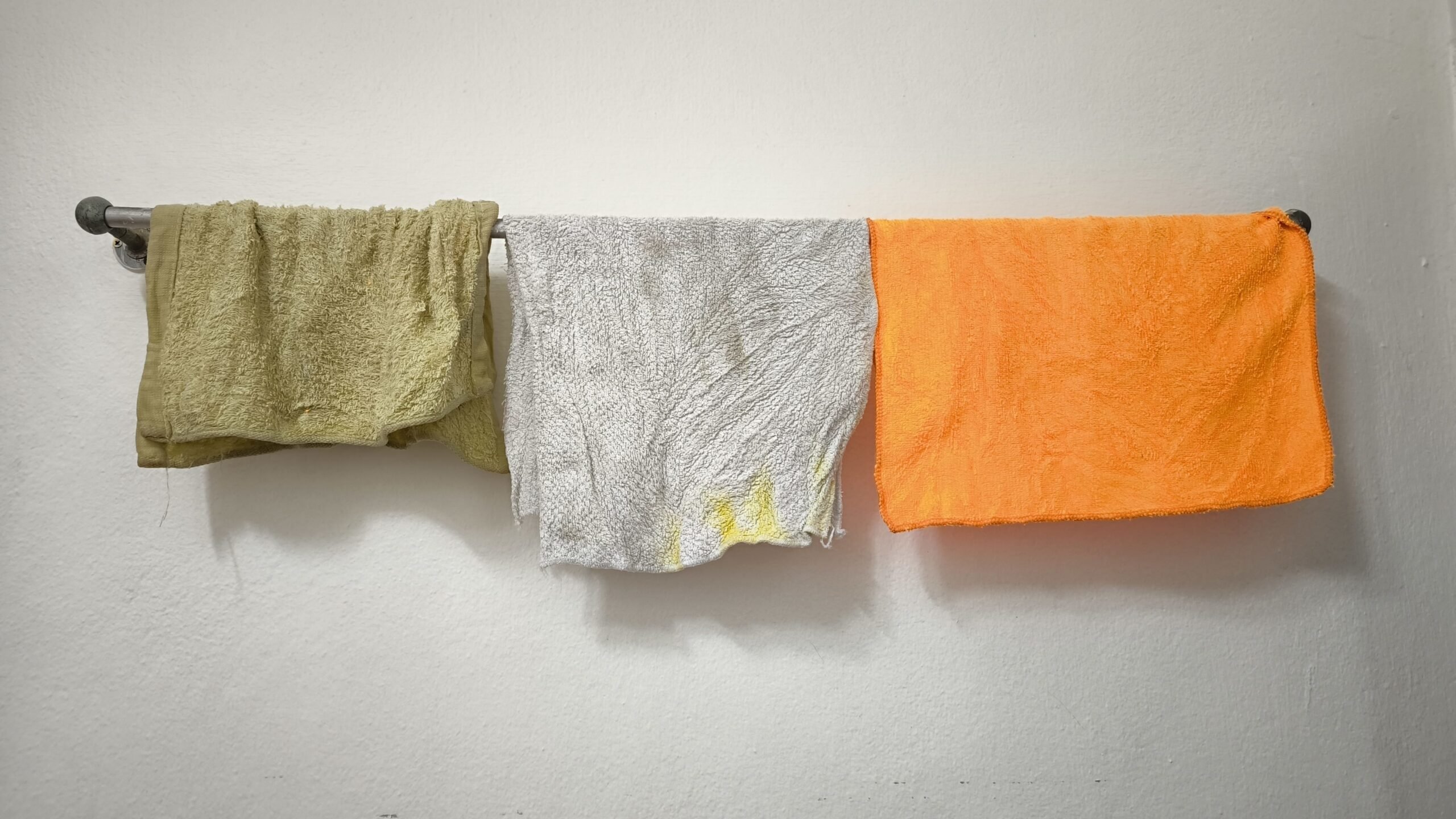 Dirty rags hanging on stainless towel hanger on white concrete wall with copy space