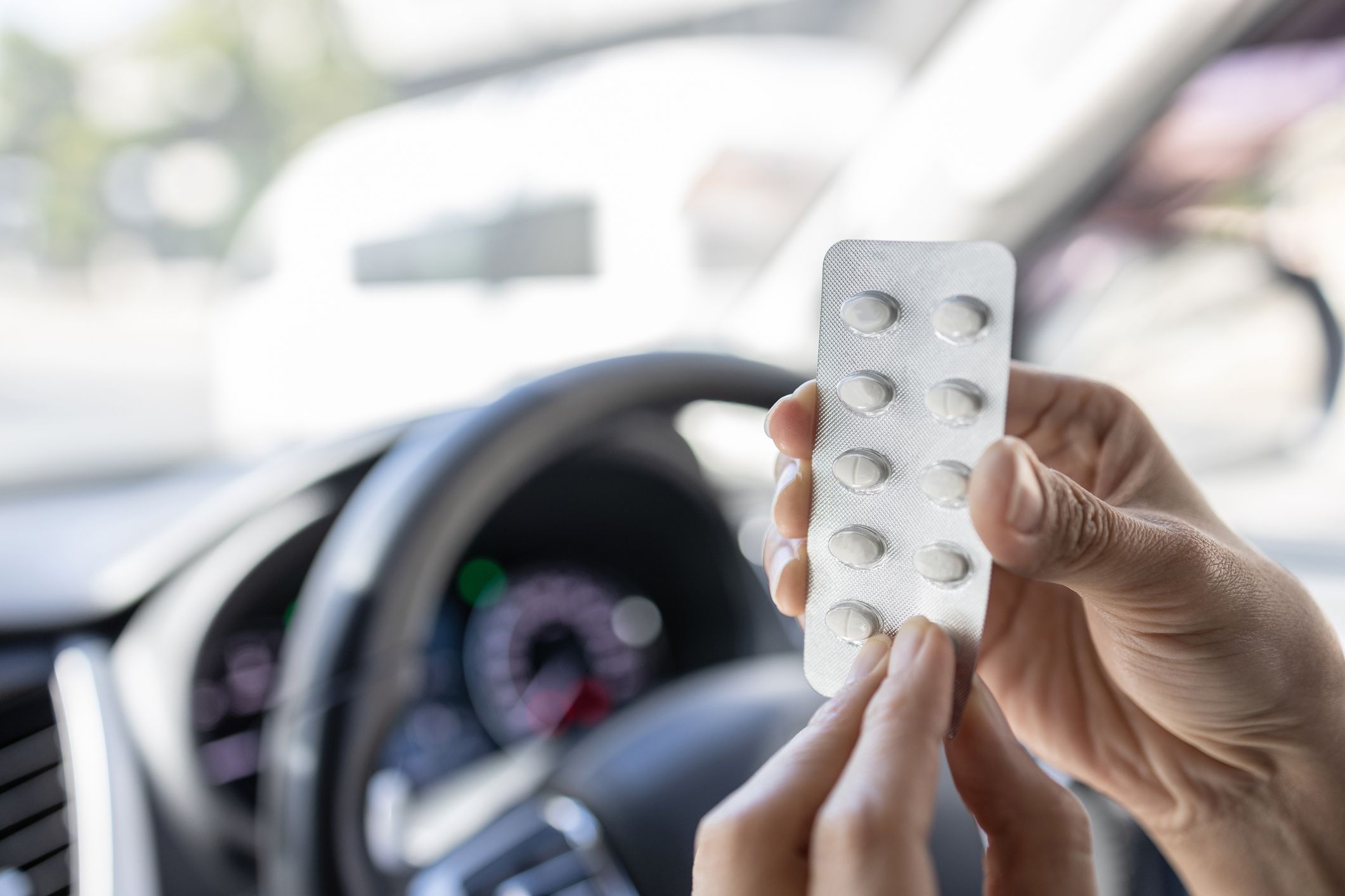 Woman holding a pill blister pack and taking medication while driving a car,dangers of consuming certain drugs that can cause drowsiness or impair focus,risk of accidents,safety on the road,safe drive