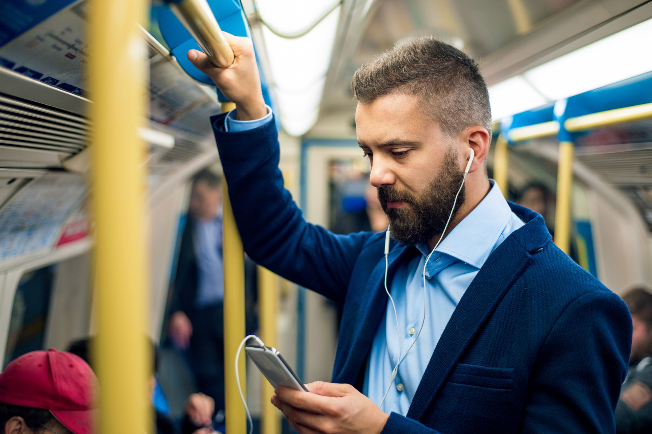 Serious businessman with headphones travelling to work. Standing inside underground wagon, holding handhandle.