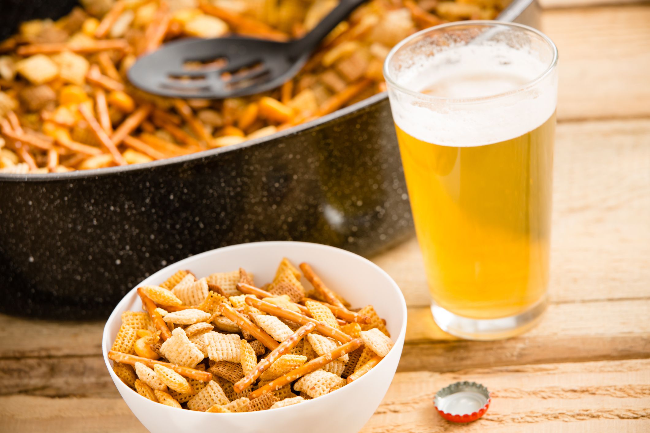 This is a shot of a cold beer sitting next to a party mix. Shot on a wooden table.