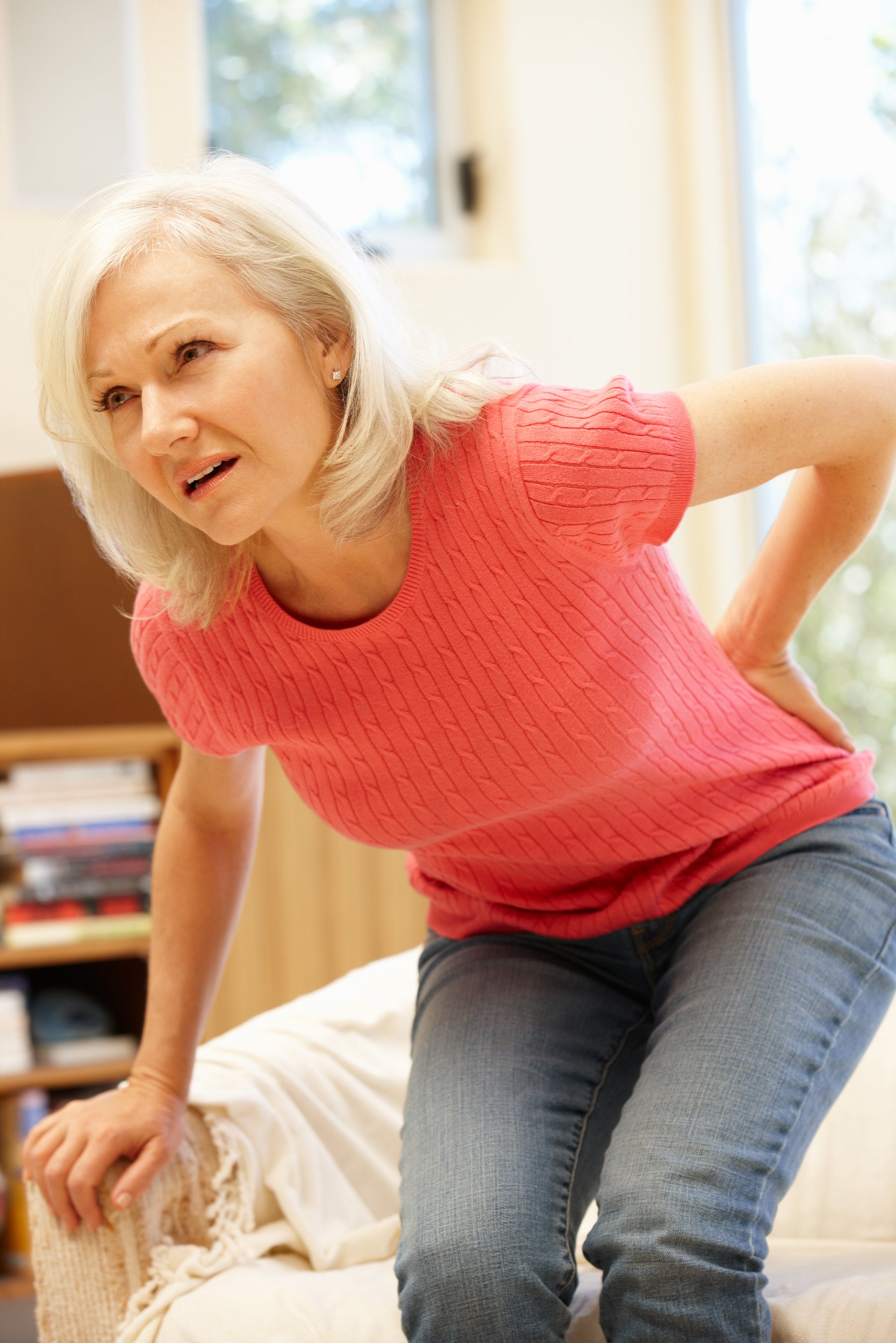 middle-aged woman getting up from couch with back pain