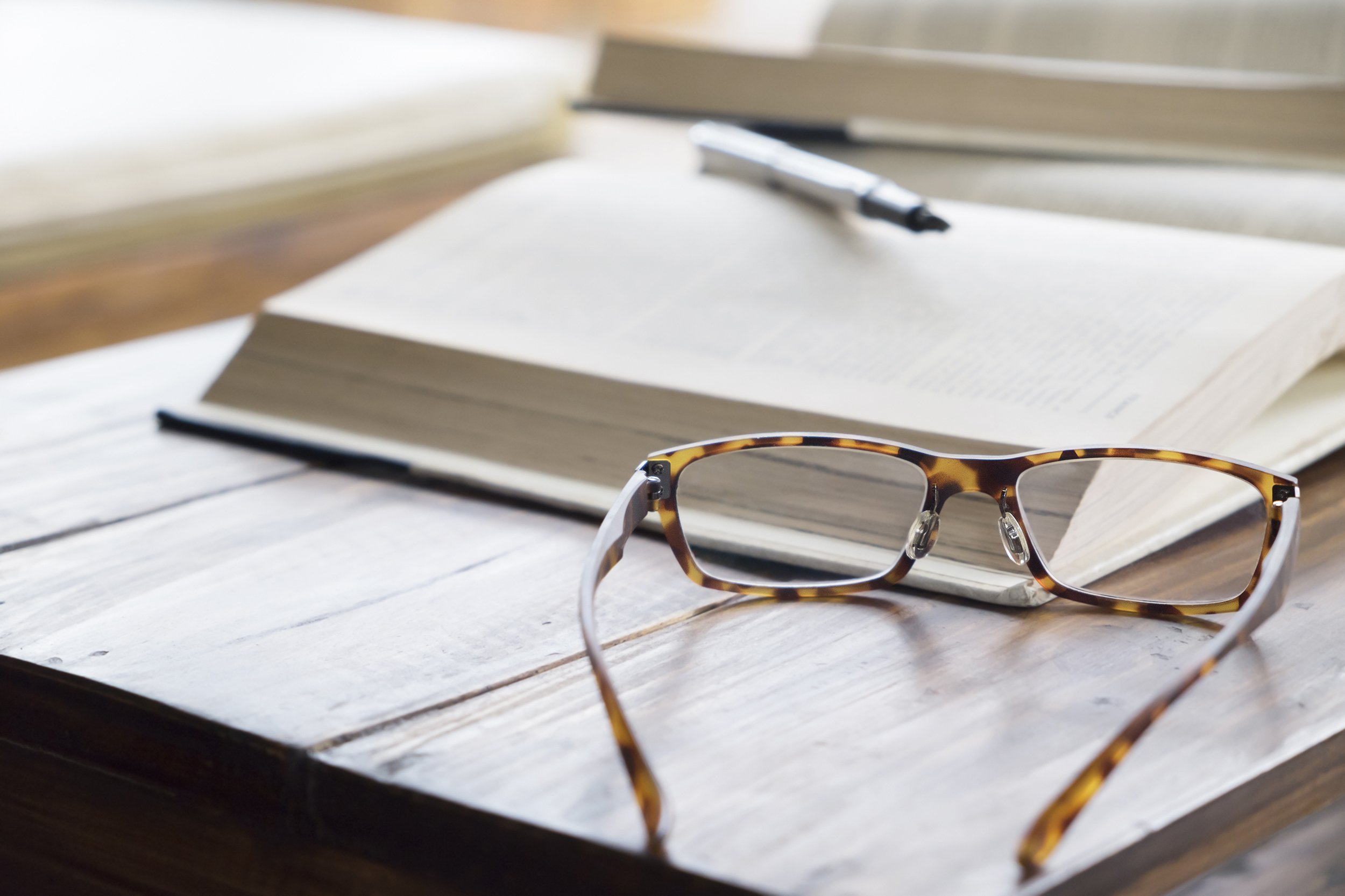 reading glasses on desk with book and pen