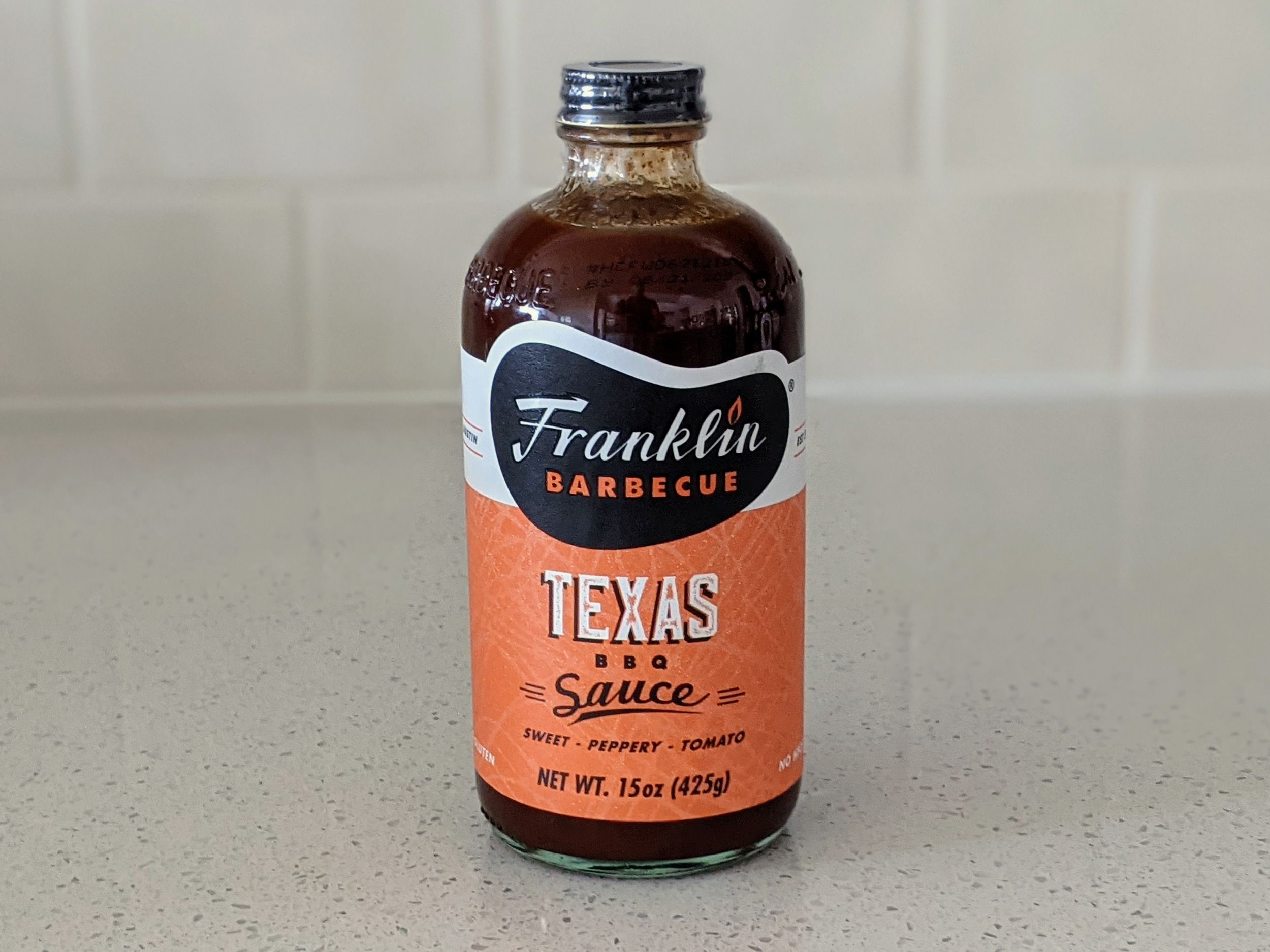 A Bottle of Franklin Barbecue Texas BBQ Sauce on a beige countertop, beige kitchen wall tile in the background