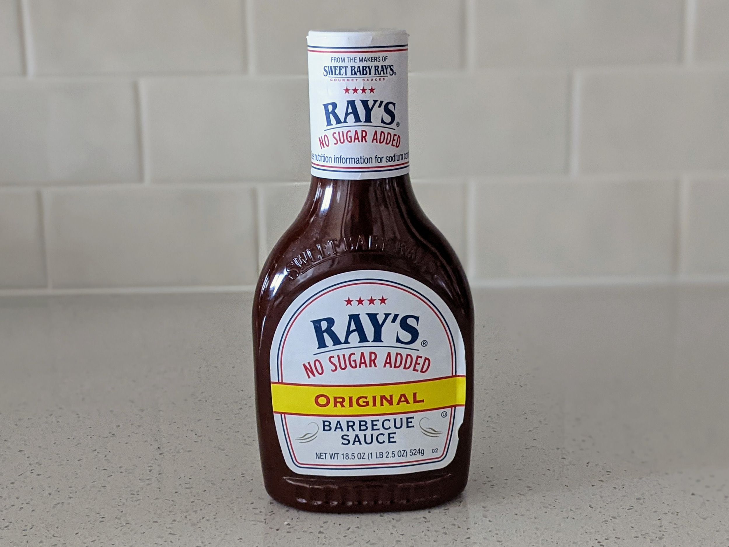 A Bottle of Ray’s No Sugar Added Original Barbecue Sauce on a beige countertop, beige kitchen wall tile in the background