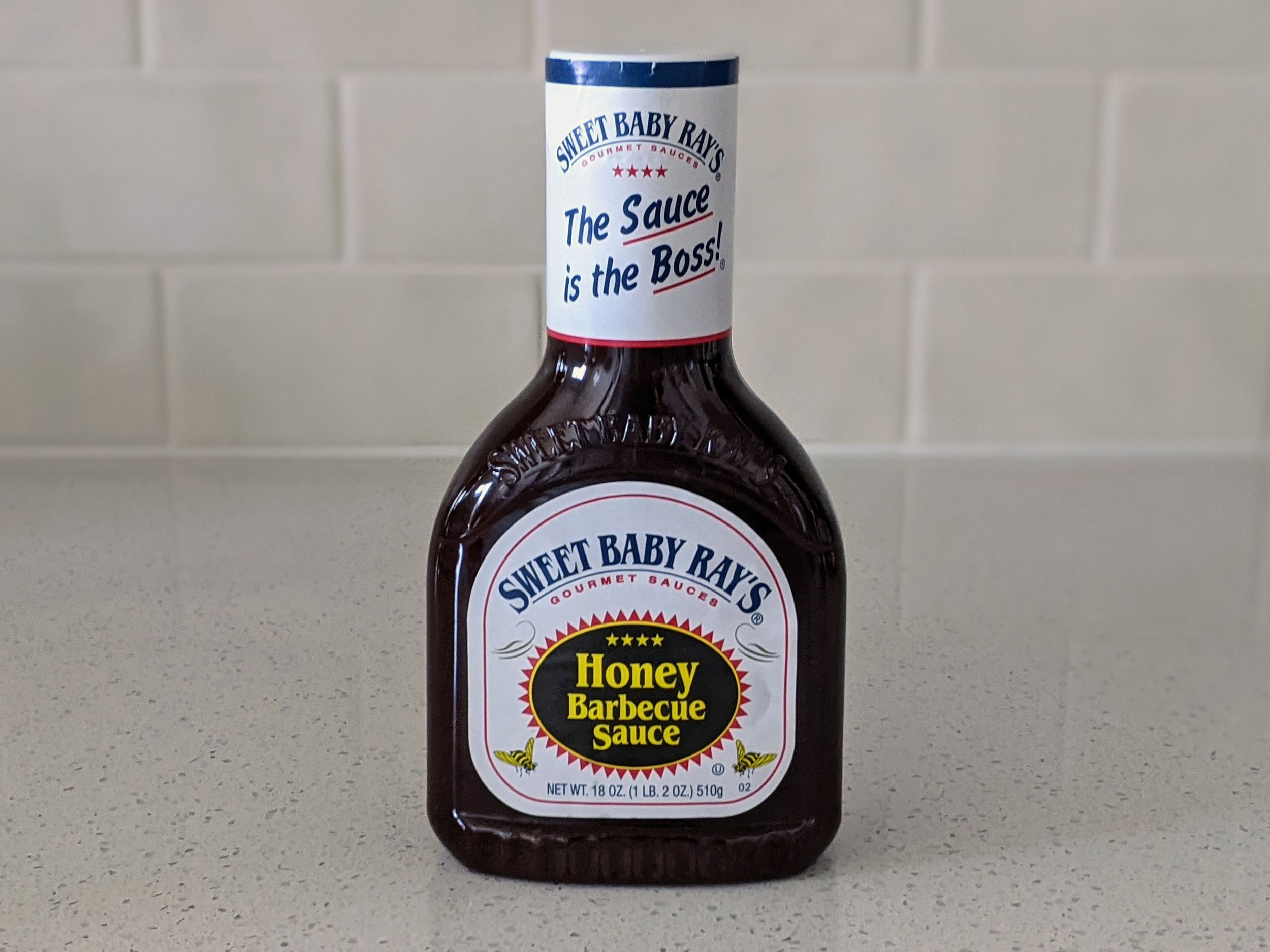 A Bottle of Sweet Baby Ray’s Honey Barbecue Sauce on a beige countertop, beige kitchen wall tile in the background