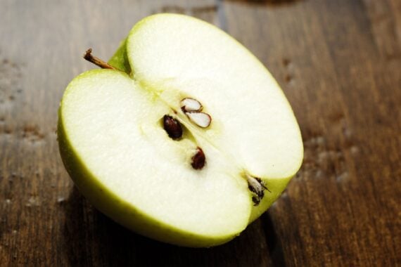 A close-up of a green apple cut in half, showing the white flesh, seeds, and stem, resting on a wooden surface.