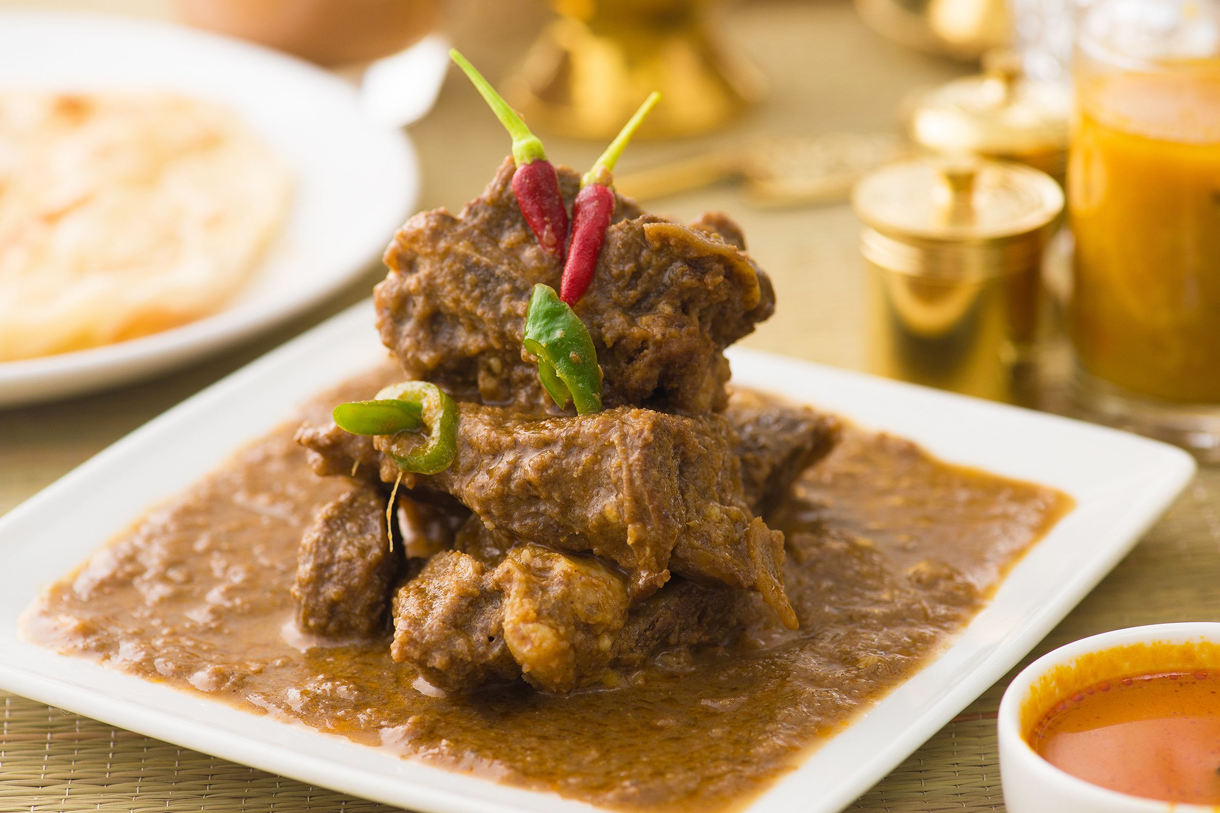 Lamb Vindaloo garnished with fresh red and green chilis served on a white square plate