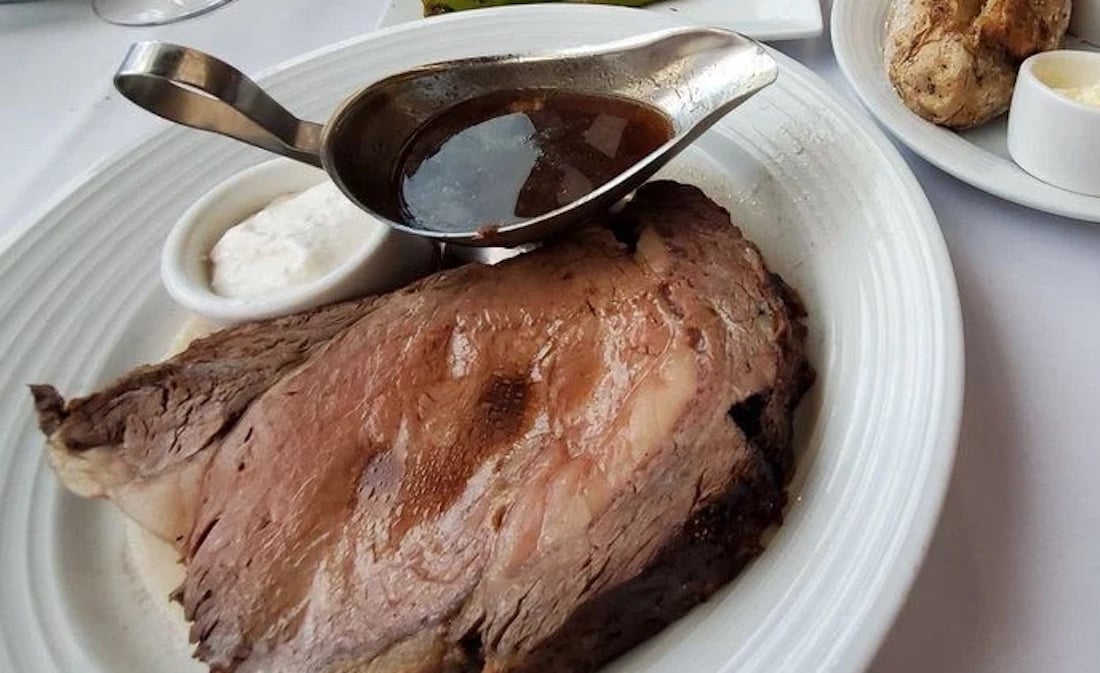 A plate with a thick slice of prime rib, a small cup of creamy horseradish sauce, and a gravy boat filled with au jus, served on a white tablecloth.