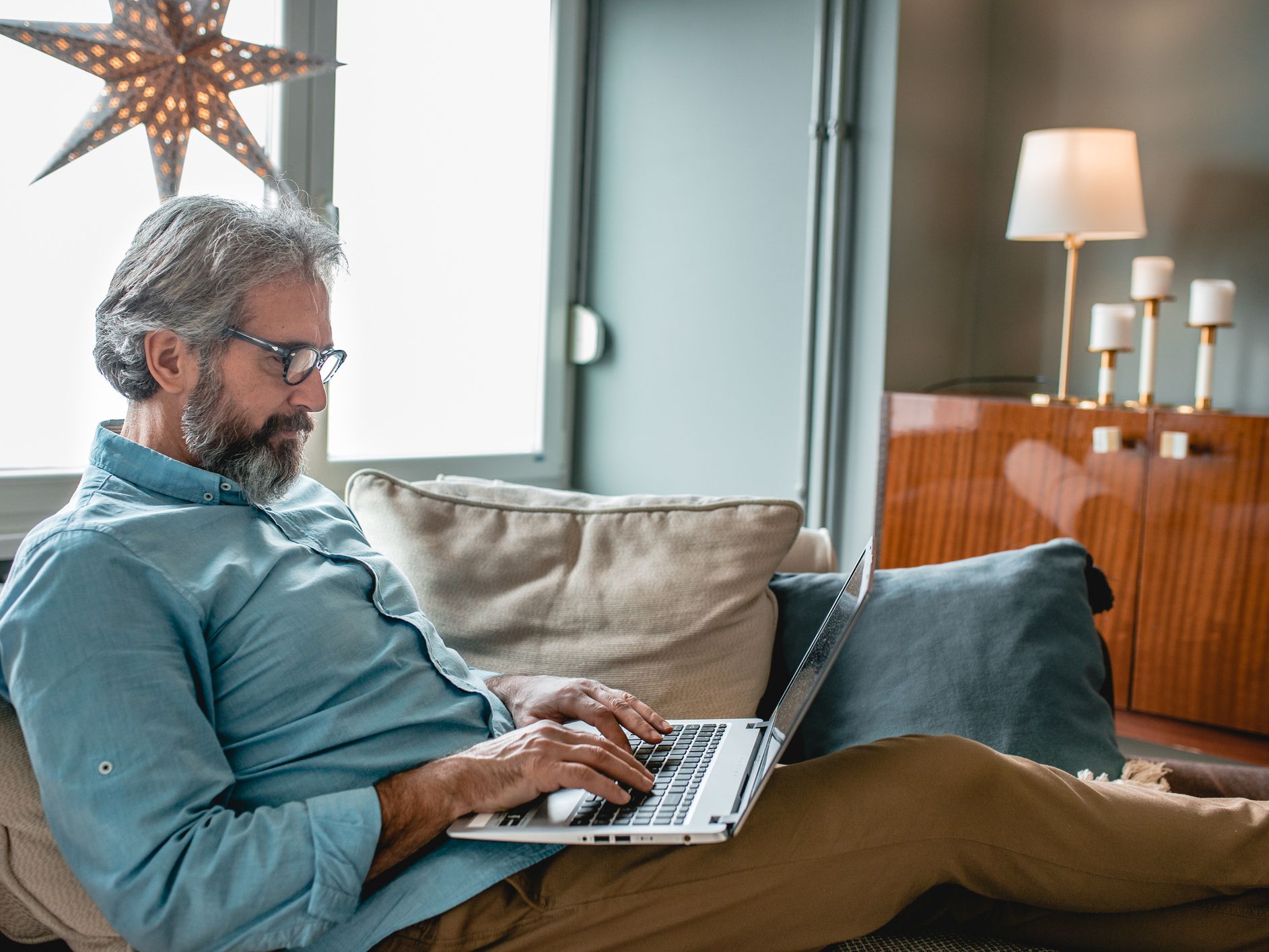 Mature good looking man sitting on sofa at home and working on a laptop