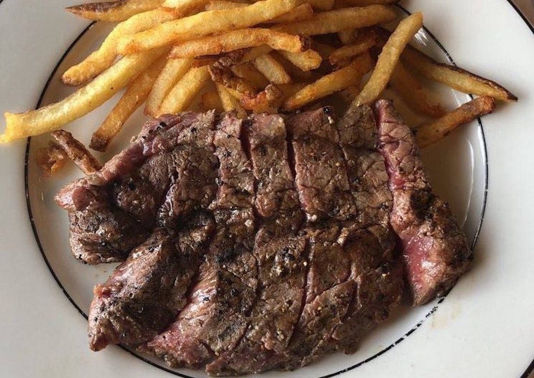 A plate with a serving of golden-brown French fries and a grilled, sliced steak seasoned with black pepper. The food is arranged on a white plate with a black rim.