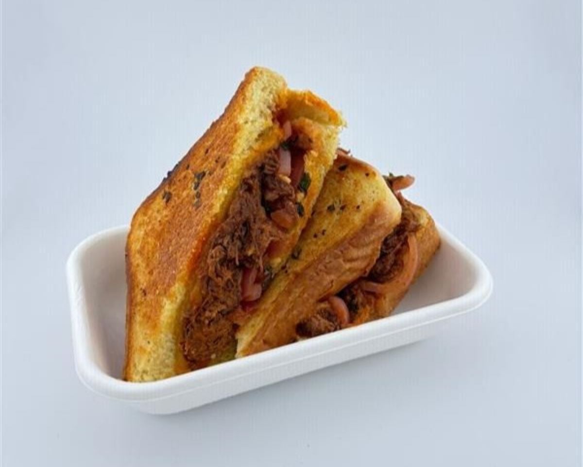 Two halves of a grilled sandwich filled with shredded meat and vegetables are placed in a white rectangular tray against a plain white background.