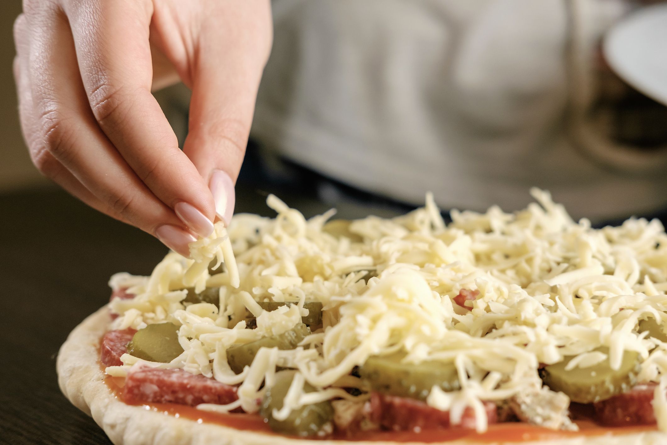 chef sprinkles cheese pizza, a lot of cheese on a pizza, cooking process, woman holding cheese in hands, close-up, homemade pizza,