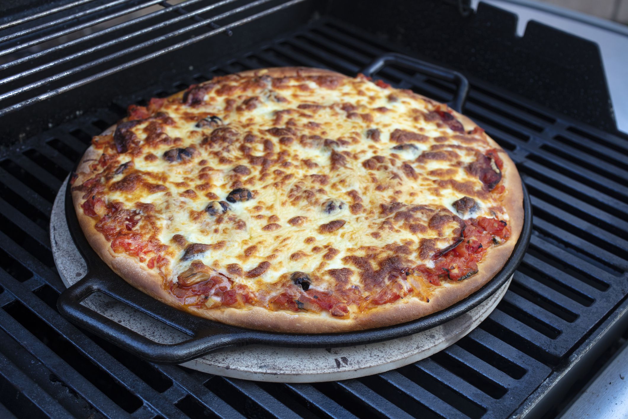 Pepperoni, cheese and tomato pizza being made on a cast iron skillet and on a barbeque grill outoors