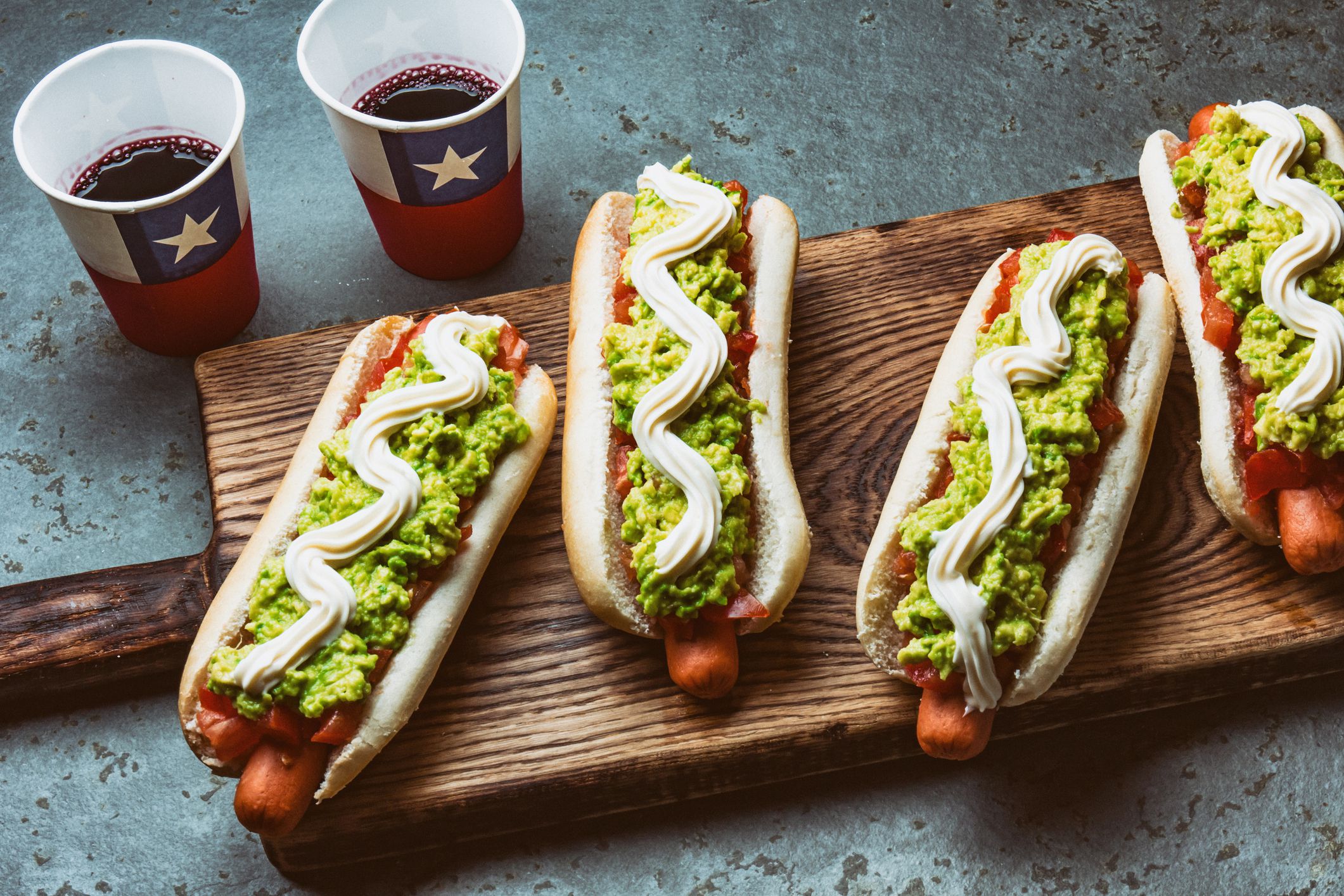 Chilean Completo Italiano. Hot dog sandwiches with tomato, avocado and mayonnaise served on wooden board with drink in paper cup . Top view. Independence Day concept.