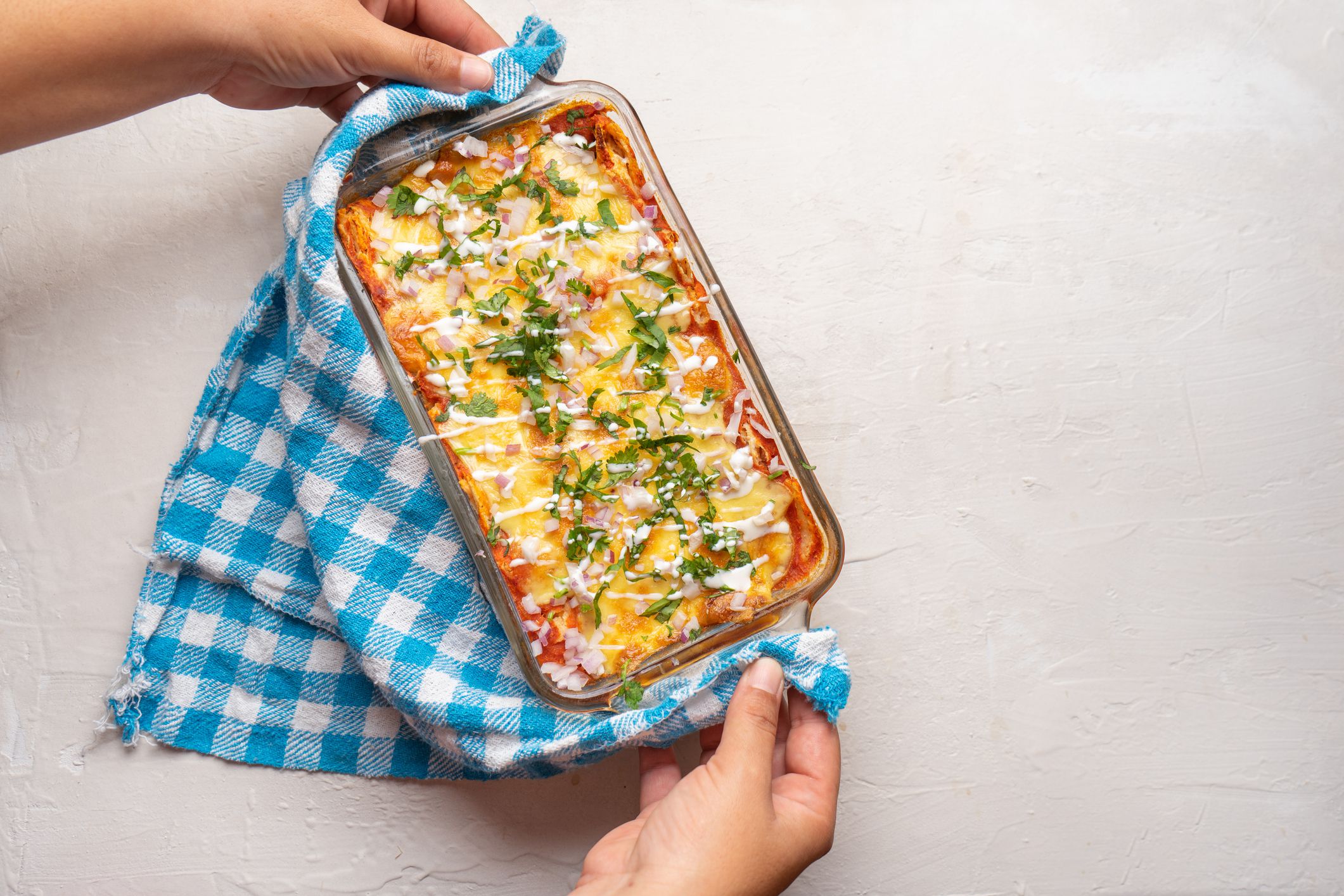 Traditional mexican red baked enchiladas with melted cheese and sour cream on white background