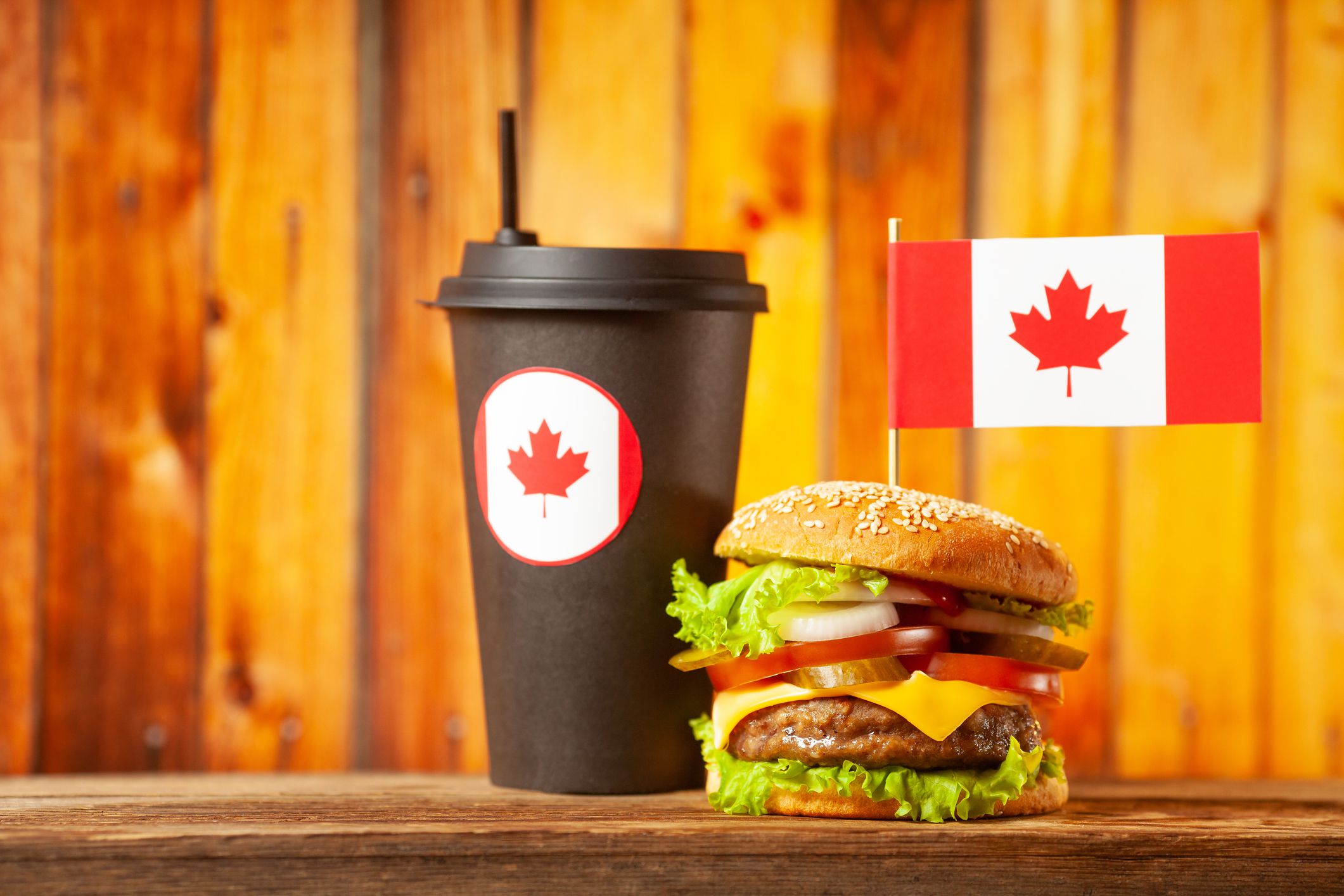 Close-up home made beef burger with Canada flag on the top and black paper cup on wooden table over wooden background.