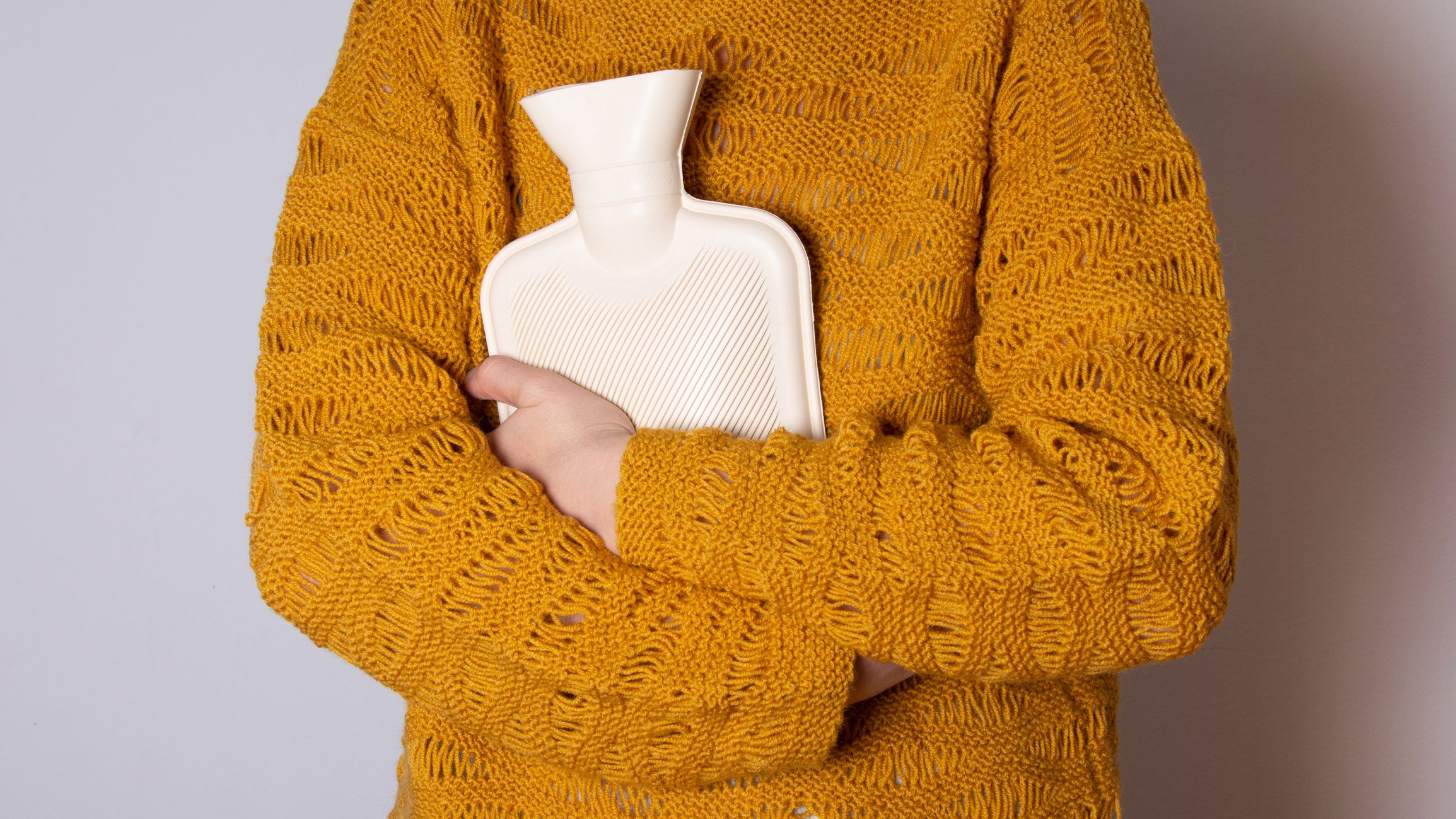 Hot water heating pad is winter essentials. Power outages and difficulties with heating. Saving electricity. Woman in orange sweater holding heating pad.