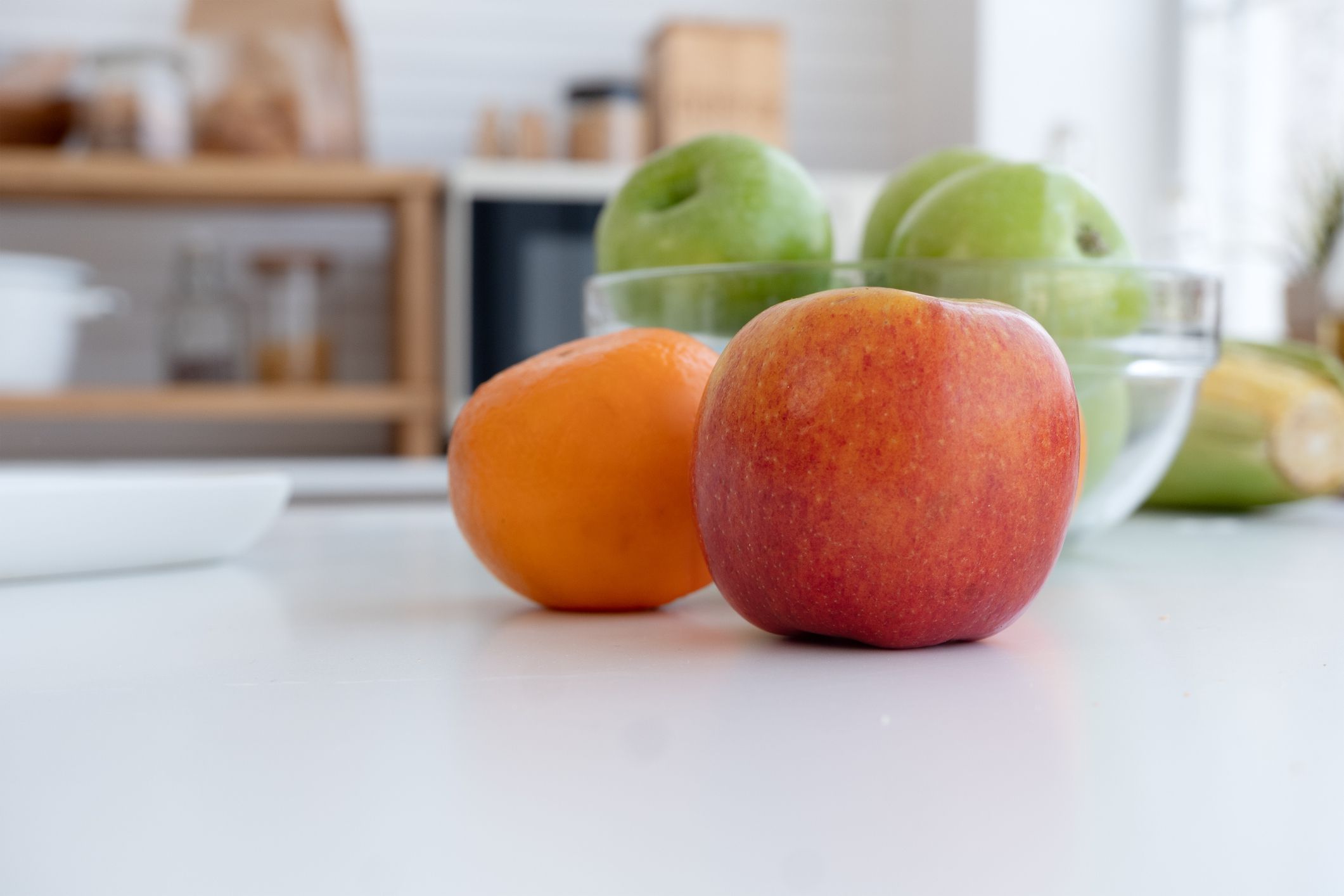 Red apple and green apple on the white table in the kitchen.