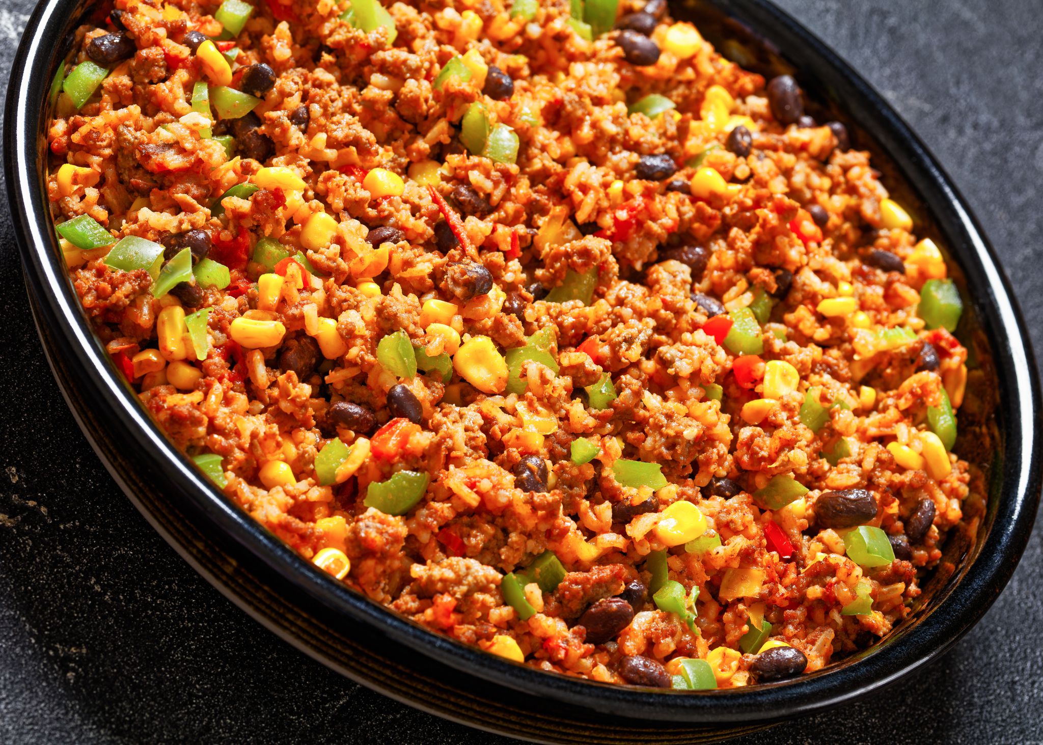 close-up of Mexican Casserole of ground beef, rice, black beans, corn, green pepper and chopped tomatoes in baking dish on concrete table