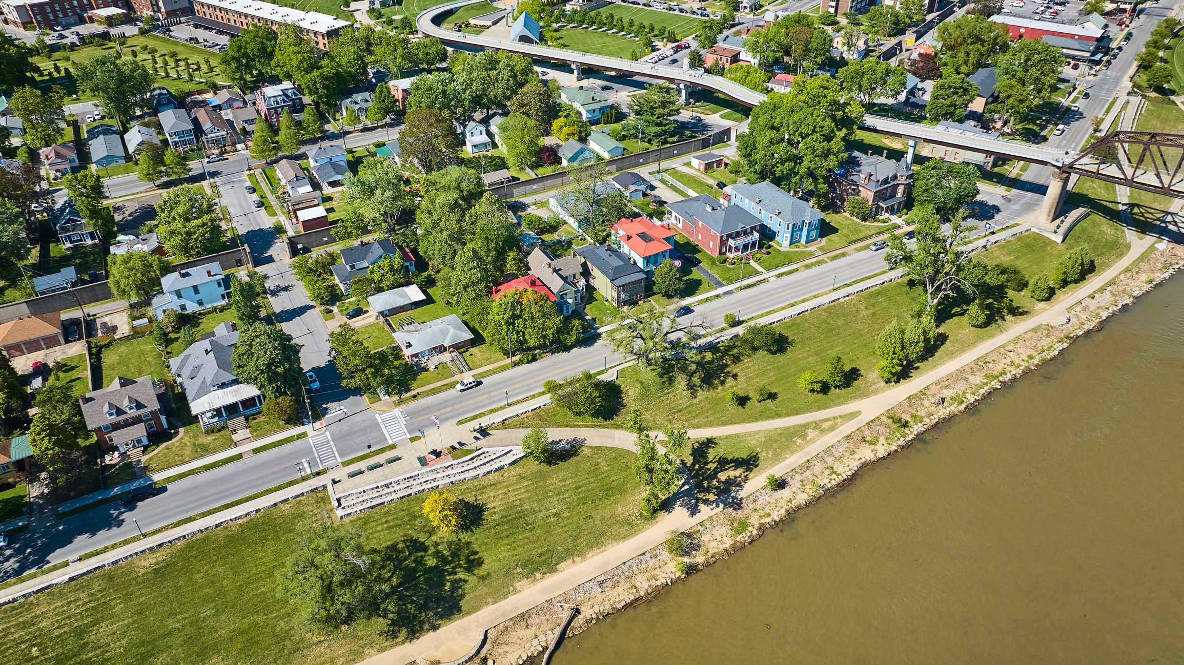 Image of Aerial city along murky brown river water houses iron arch bridge suspended highway roads