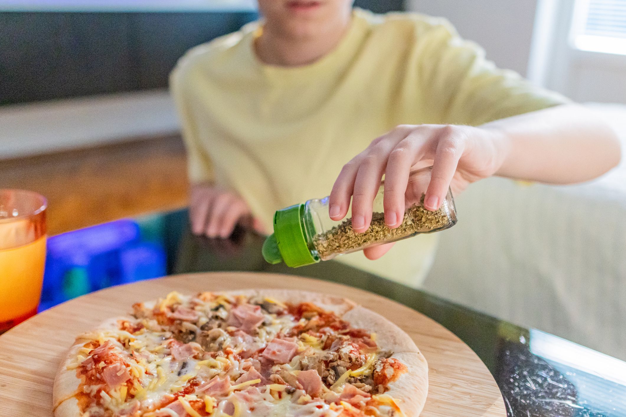 Cute boy is enjoying a slice of pizza at home. He is adding spices on pizza.