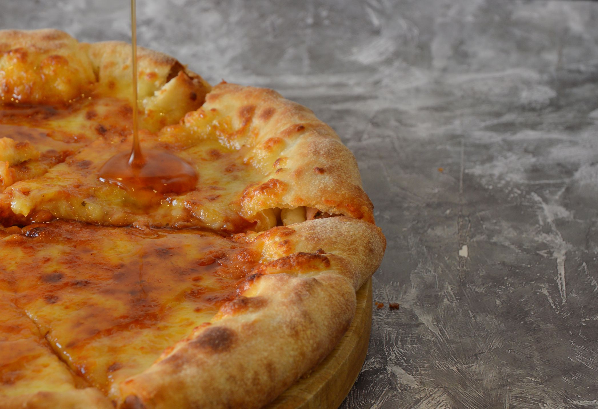 Pouring natural honey to a delicious cheese pizza with sausage crust