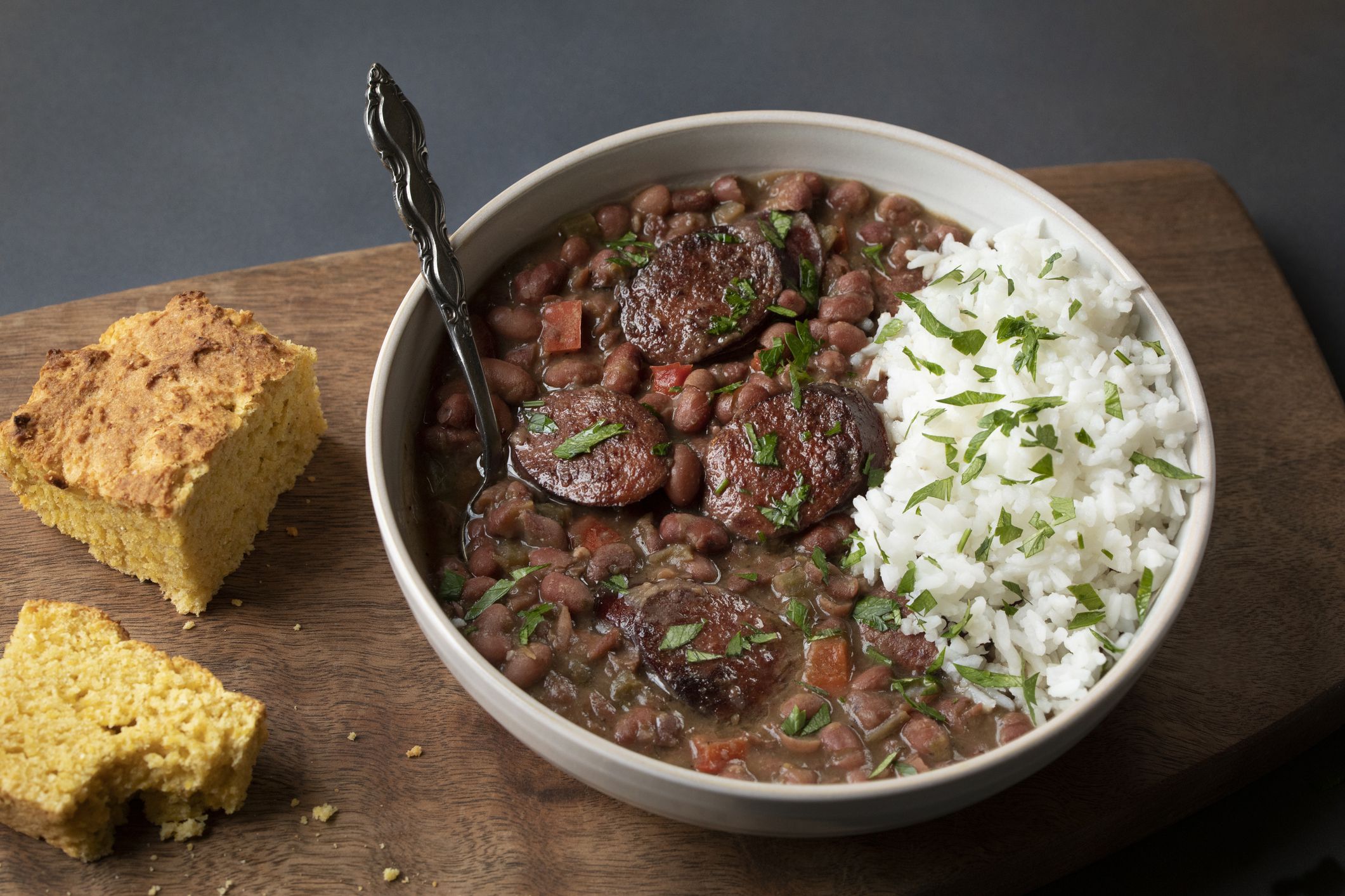 CLASSIC RED BEANS AND RICE WITH ANDOUILLE SAUSAGE, CILANTRO AND CORNBREAD ON A WOODEN BOARD WITH SPOON