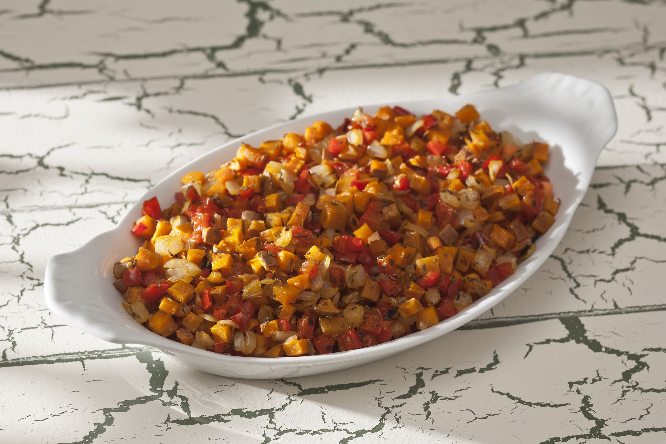 Sweet Potato Hash (Sweet Potatoes, Red Pepper and Onion) in white dish on cream and green distressed surface.