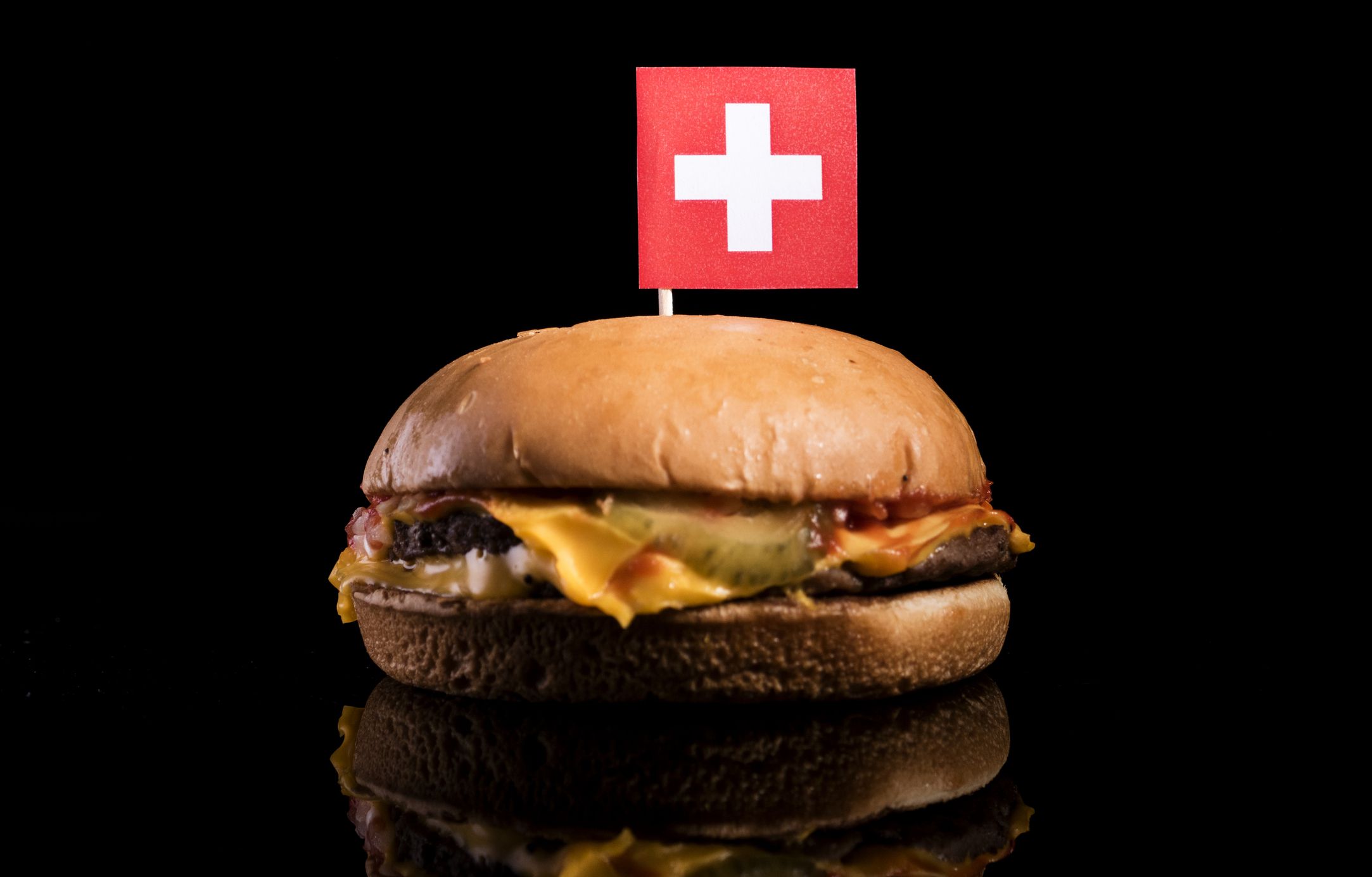 Swiss flag on top of hamburger isolated on black background
