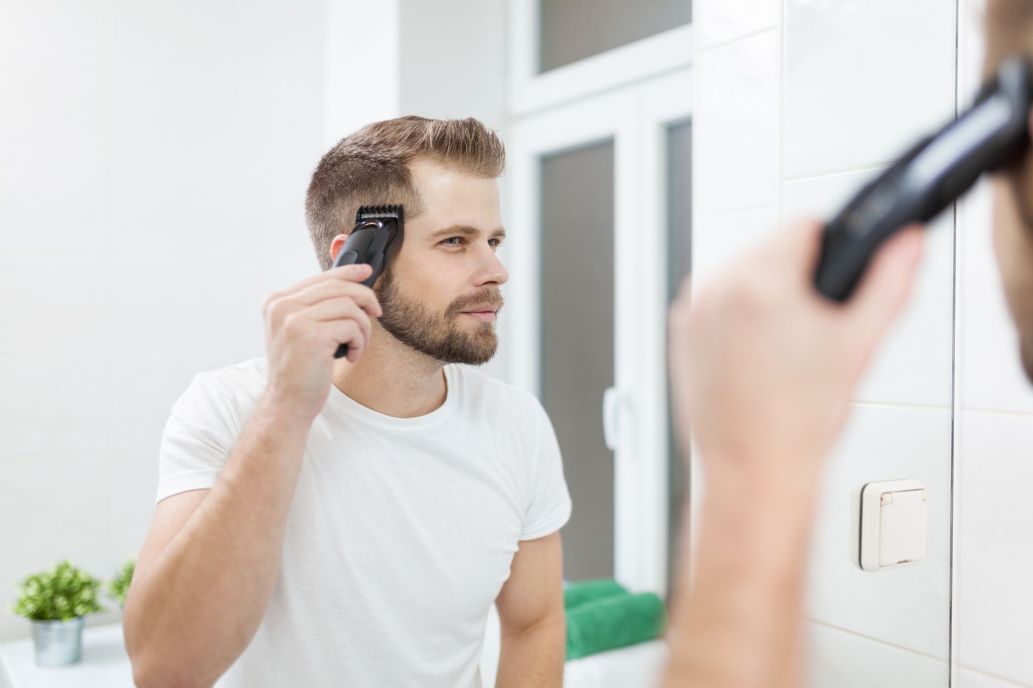 Handsome bearded man cutting his own hair with a clipper