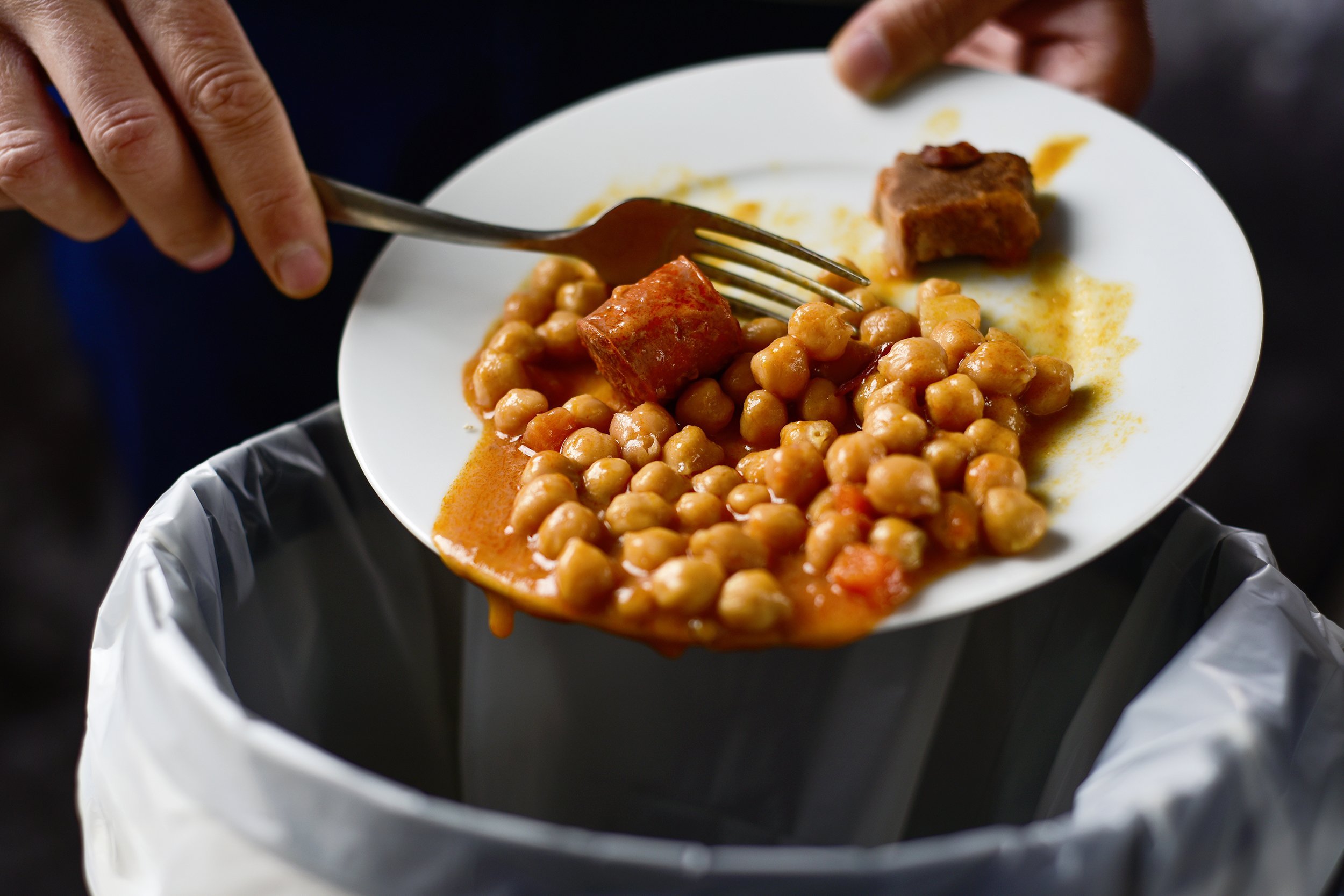 man throwing the leftover of a plate of chickpea stew to the trash bin