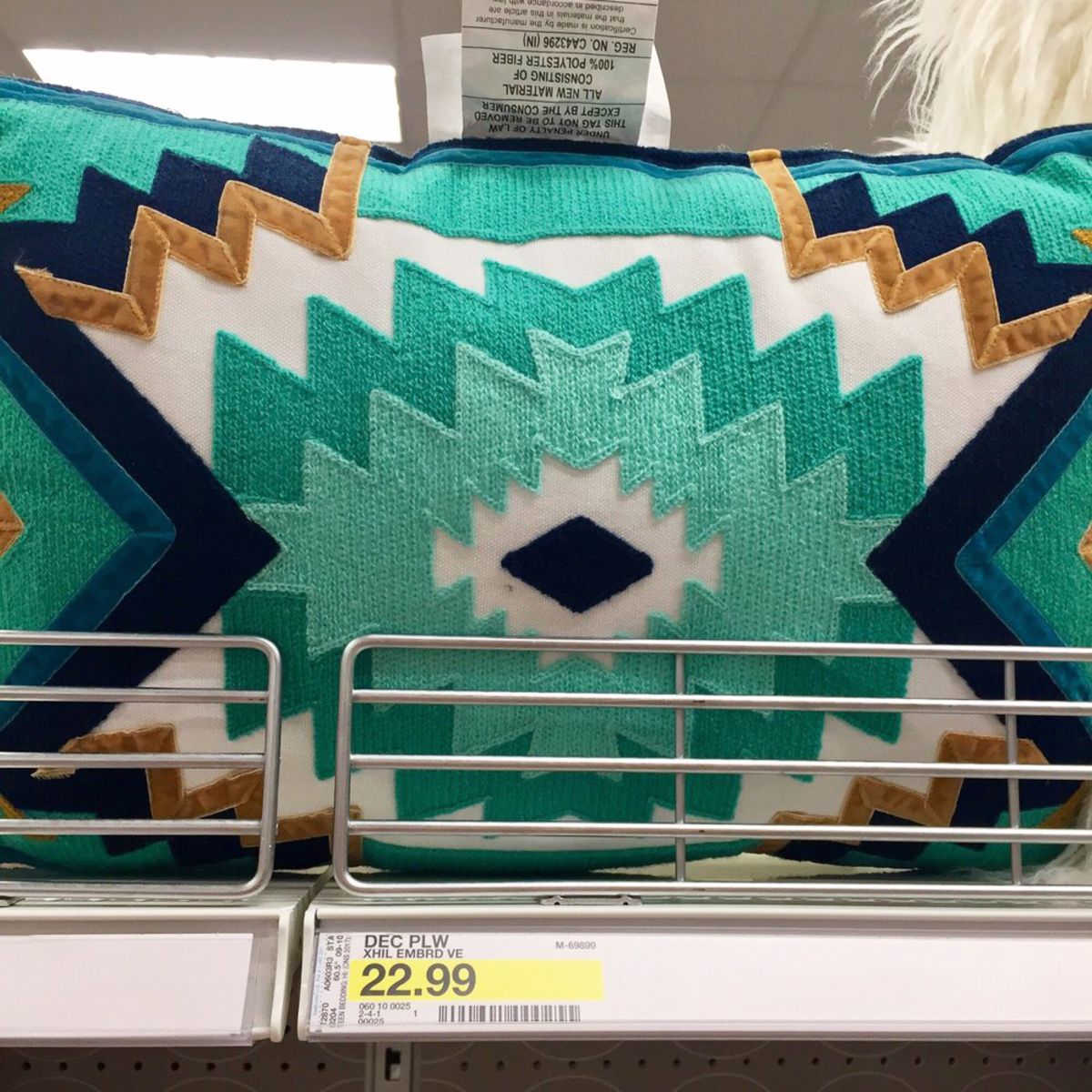 A large aqua geometric Native American style accent pillow on a shelf at a Target store, lights on the ceiling in the top background