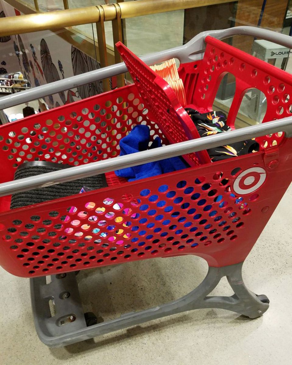 A red plastic cart filled with a few items at a Target store, beige floor and brass railing in the background