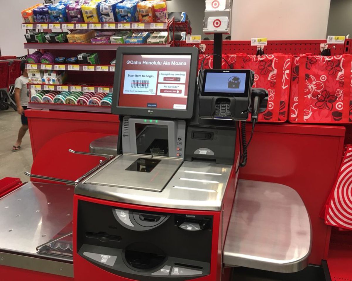 A self-checkout at a Target store, many types of gum for sale on the top left and red reusable bags on the top right